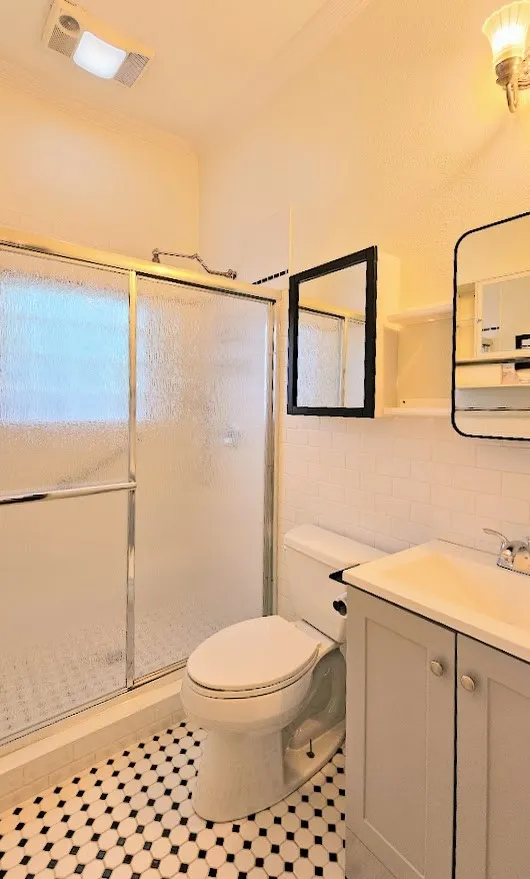 Bathroom featuring a glass-enclosed shower, white subway tile accents, a black and white hexagon tile floor, a vanity with a rectangular sink, and a mirrored medicine cabinet