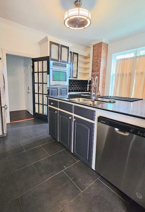 Kitchen featuring dark-toned cabinetry, stainless steel appliances, a subway tile backsplash, and dark tile flooring