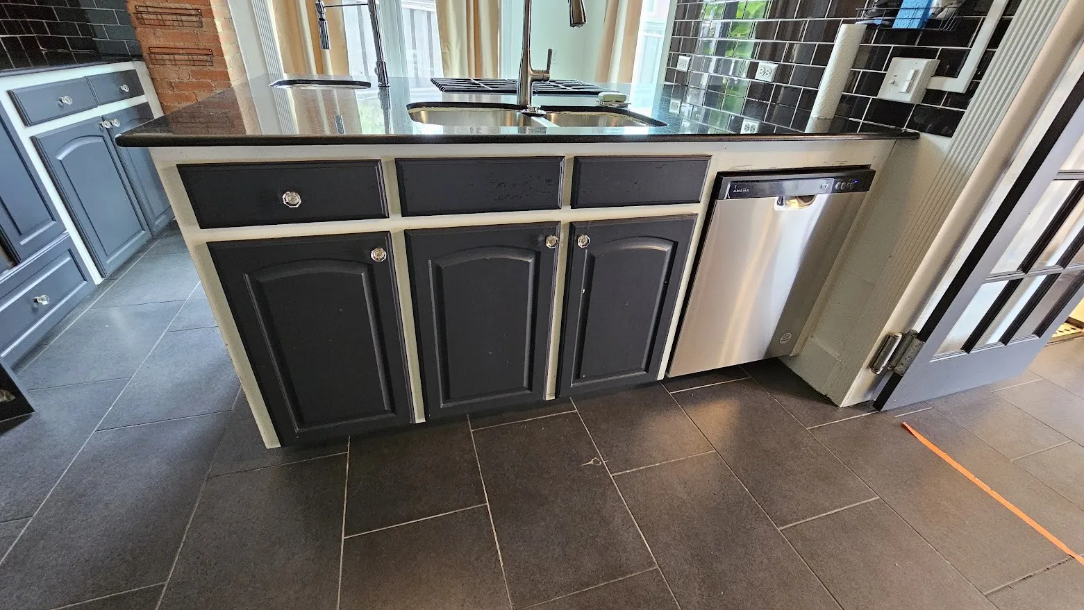 Kitchen island featuring dark cabinetry with white trim, dark countertop, and integrated stainless steel dishwasher