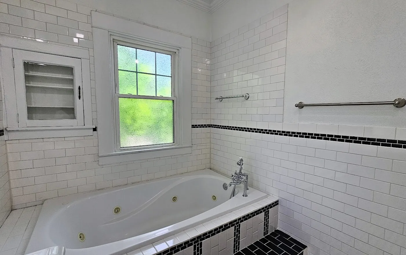 Jetted soaking tub with a deck-mounted faucet, surrounded by white subway tile with a black mosaic tile accent band