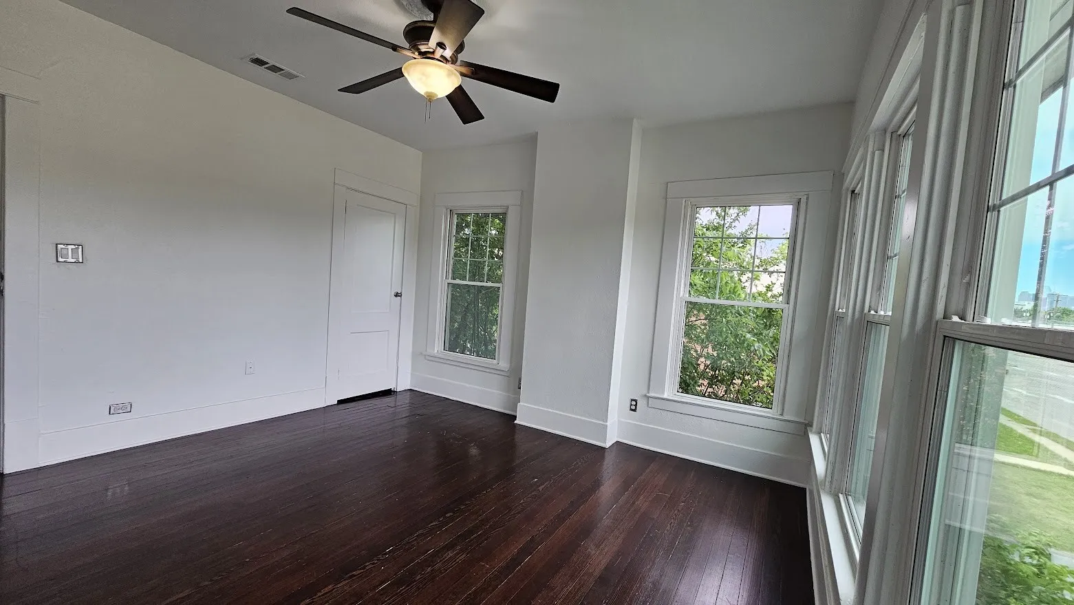 Bright room featuring dark wood-finish flooring, crisp white walls, and multiple windows
