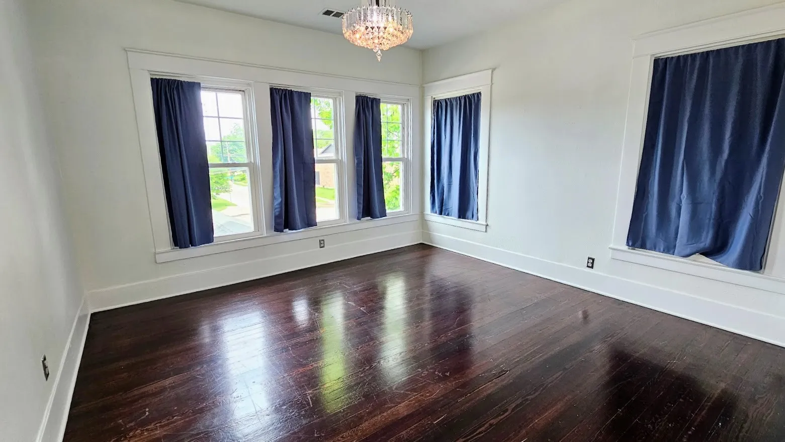 Spacious room featuring rich wood-finish flooring, white trim, and a crystal chandelier