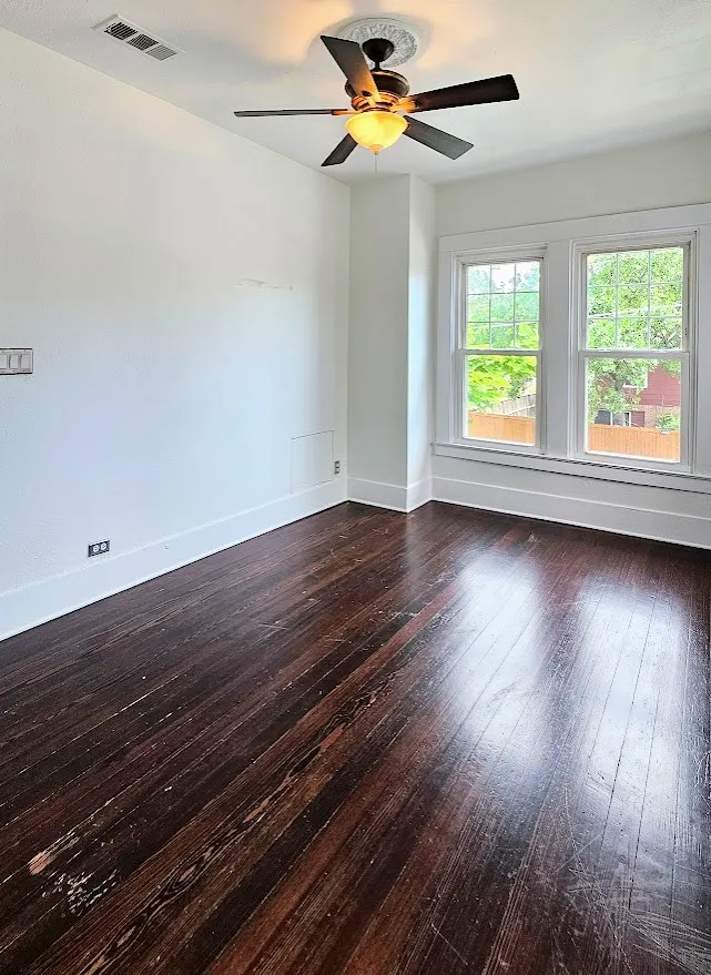 Spacious room featuring dark wood-finish flooring, bright white walls, and a ceiling fan with an ornamental medallion