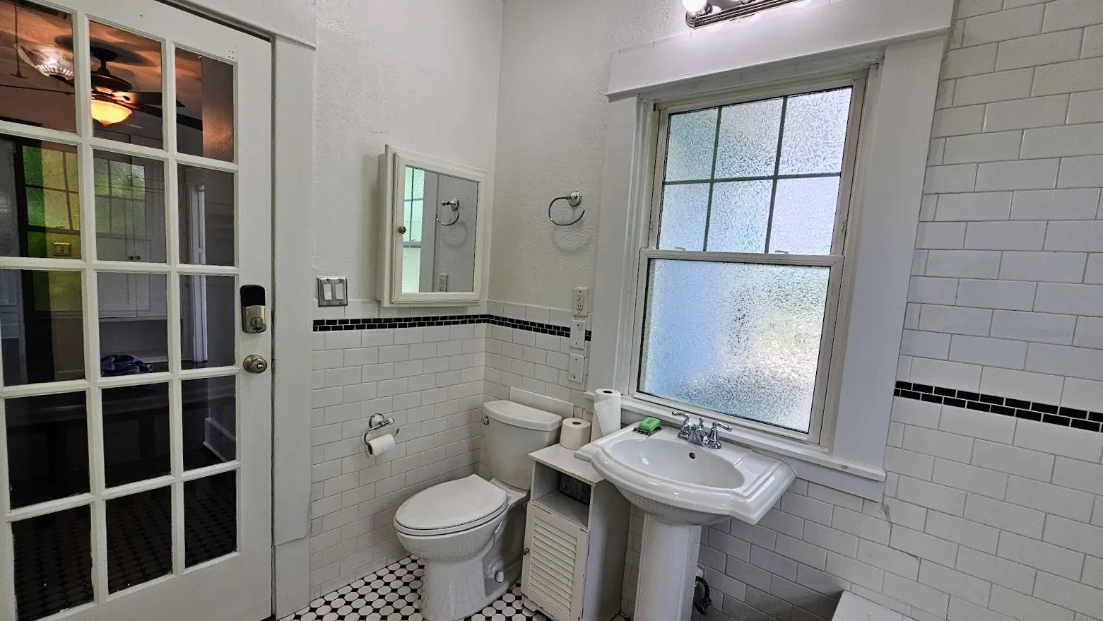 Bathroom featuring white subway tile wainscoting with black accent tile, a pedestal sink, and a framed medicine cabinet
