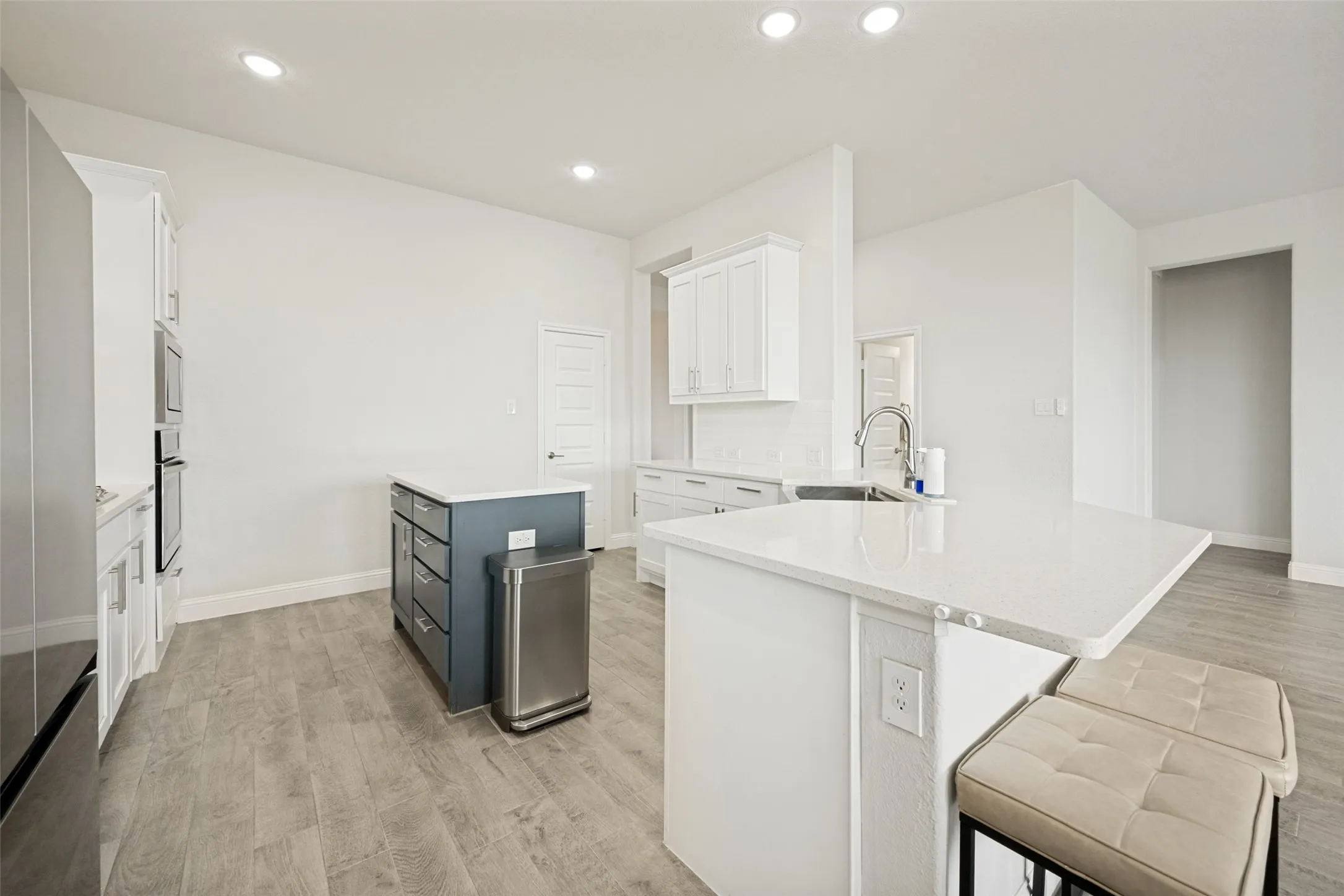 Contemporary kitchen featuring an oversized island with countertop seating, white shaker cabinetry, stainless steel appliances, and wood-finish flooring