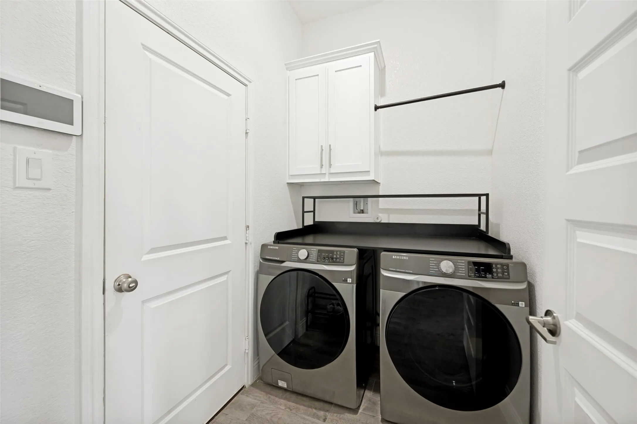 Dedicated laundry area featuring a white shaker-style wall cabinet, a black drying rack, and a counter surface above the appliances