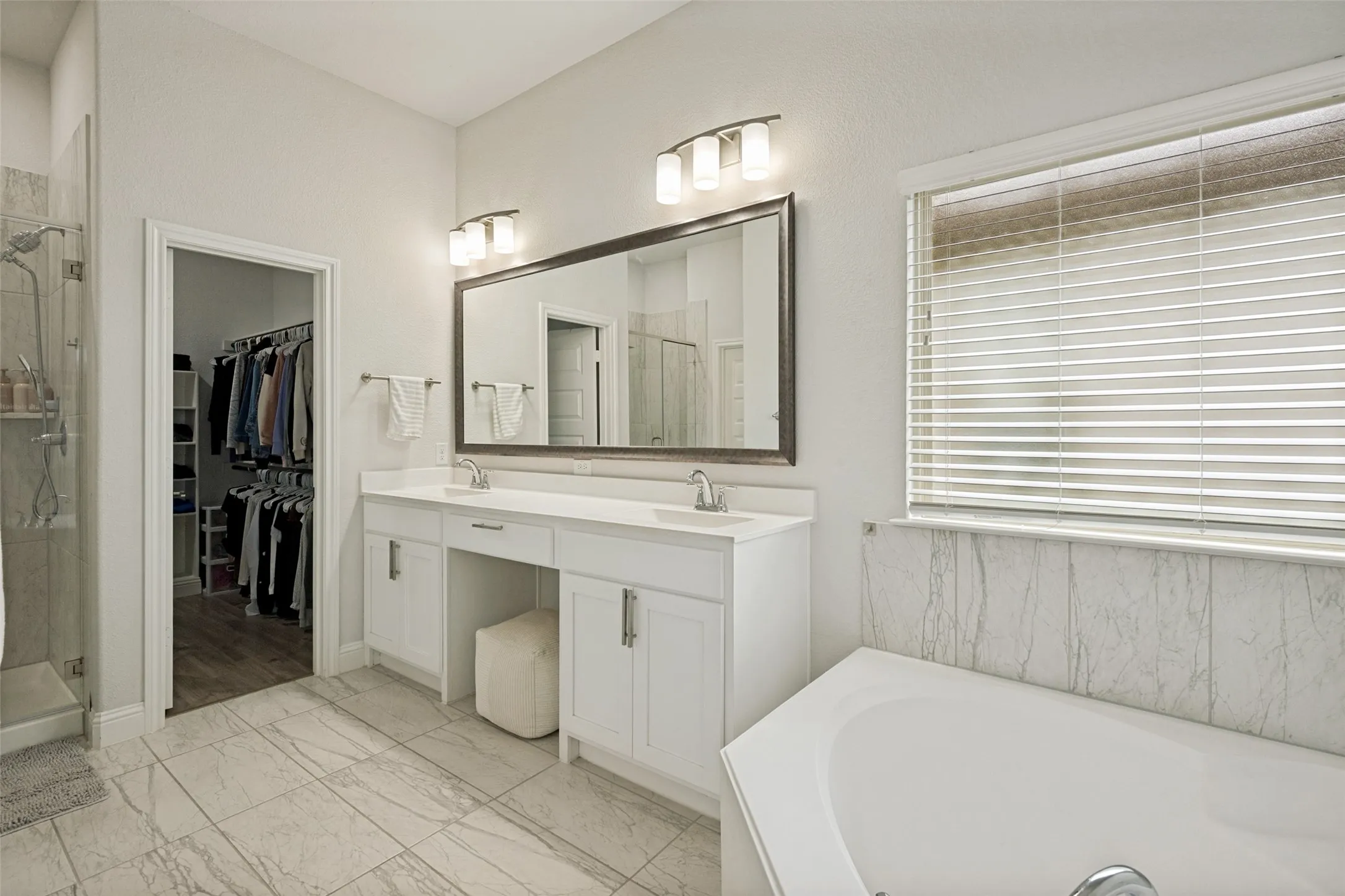 Primary Bathroom featuring a double vanity with undermount sinks and white cabinetry, a large mirrored wall, and a built-in soaking tub