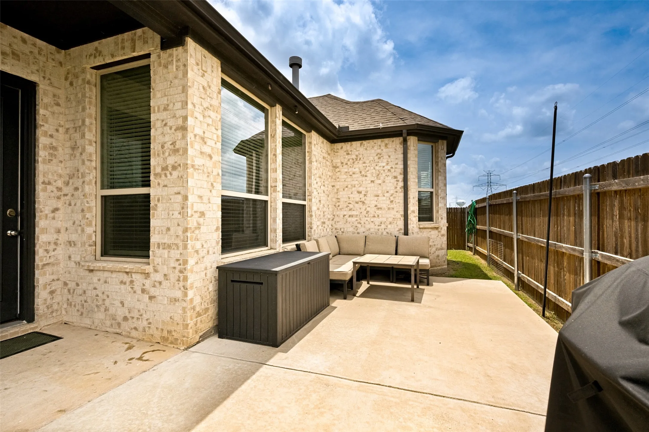 Private concrete patio featuring light brick exterior, a dark brown wood fence, and mature landscaping