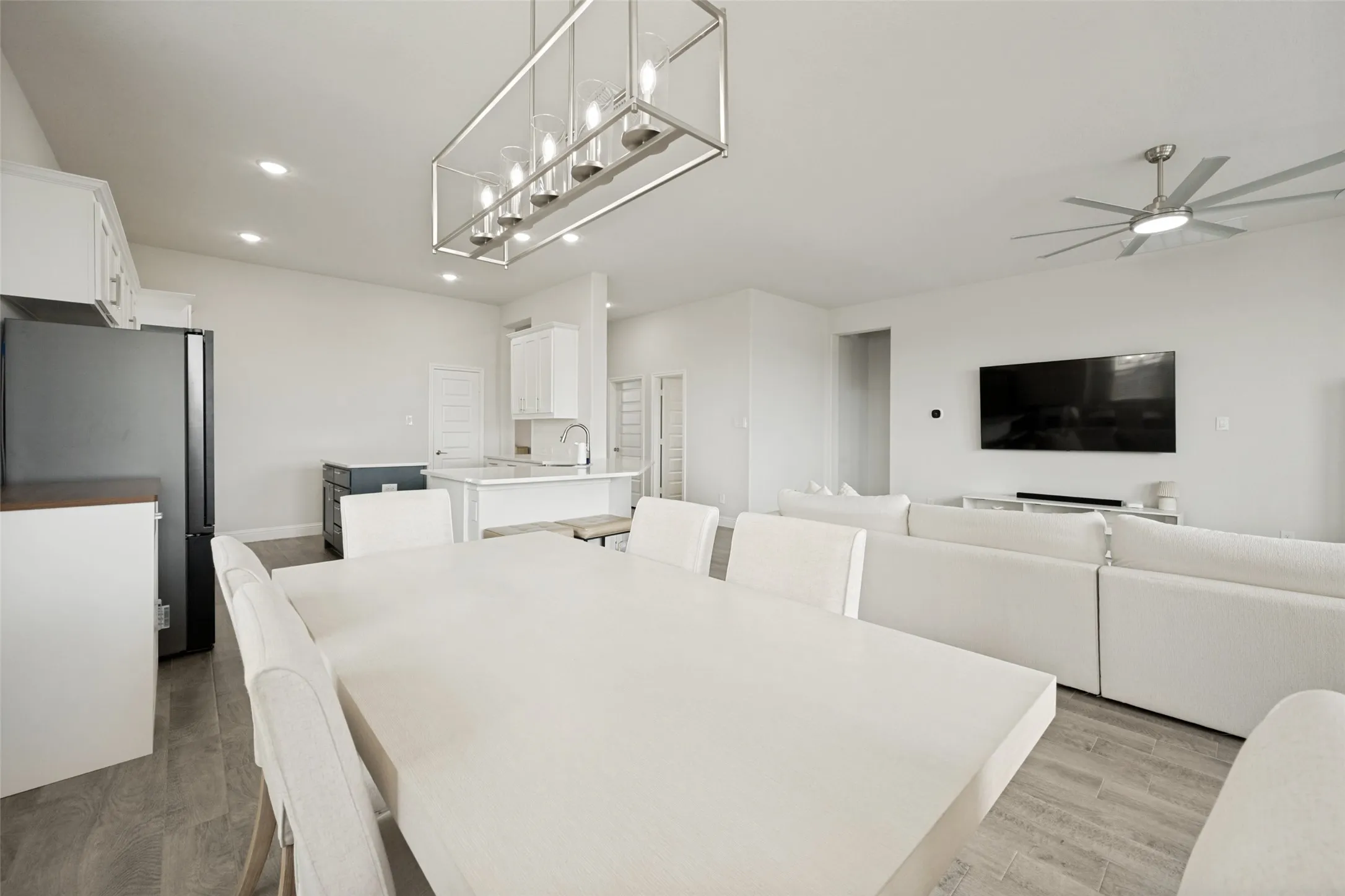 Open-concept living space featuring wood-finish flooring, a contemporary linear chandelier, recessed lighting, and a kitchen island with a sink
