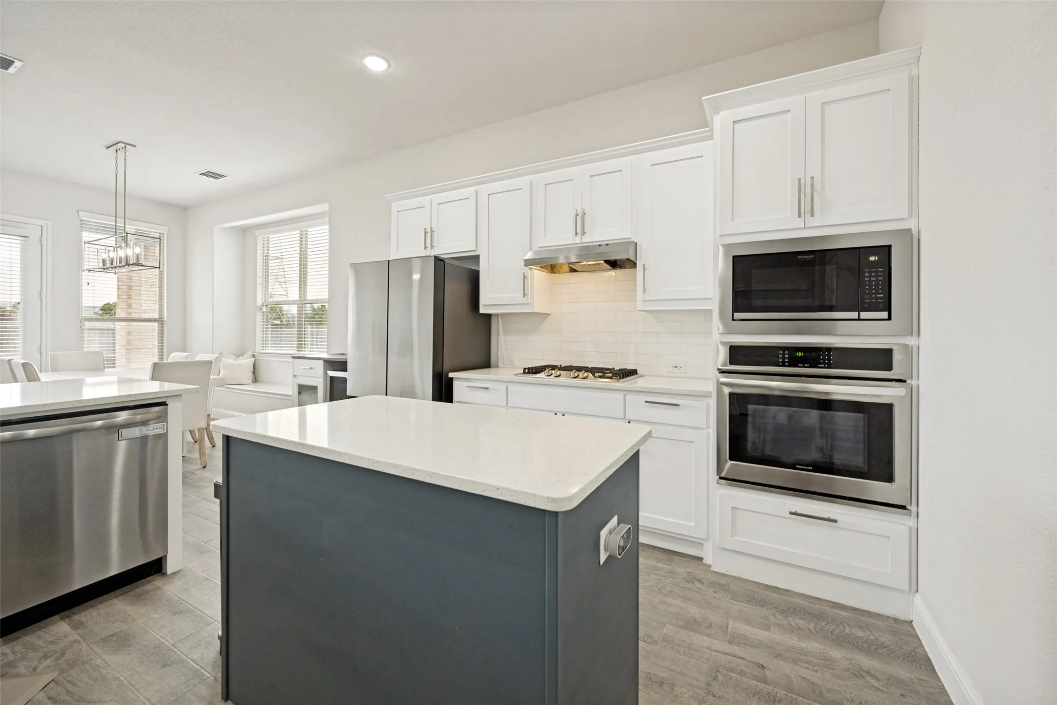 Modern kitchen featuring a central island with a light-colored countertop, white cabinetry, built-in stainless steel oven and microwave, and wood-finish flooring