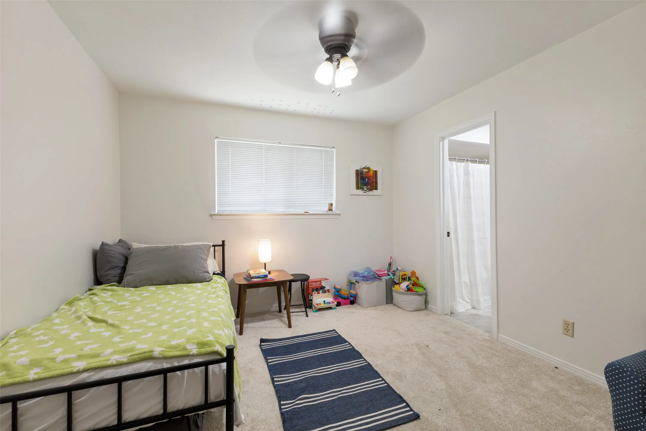 Carpeted room featuring a ceiling fan with integrated lighting, a window with blinds, and an entryway to another space