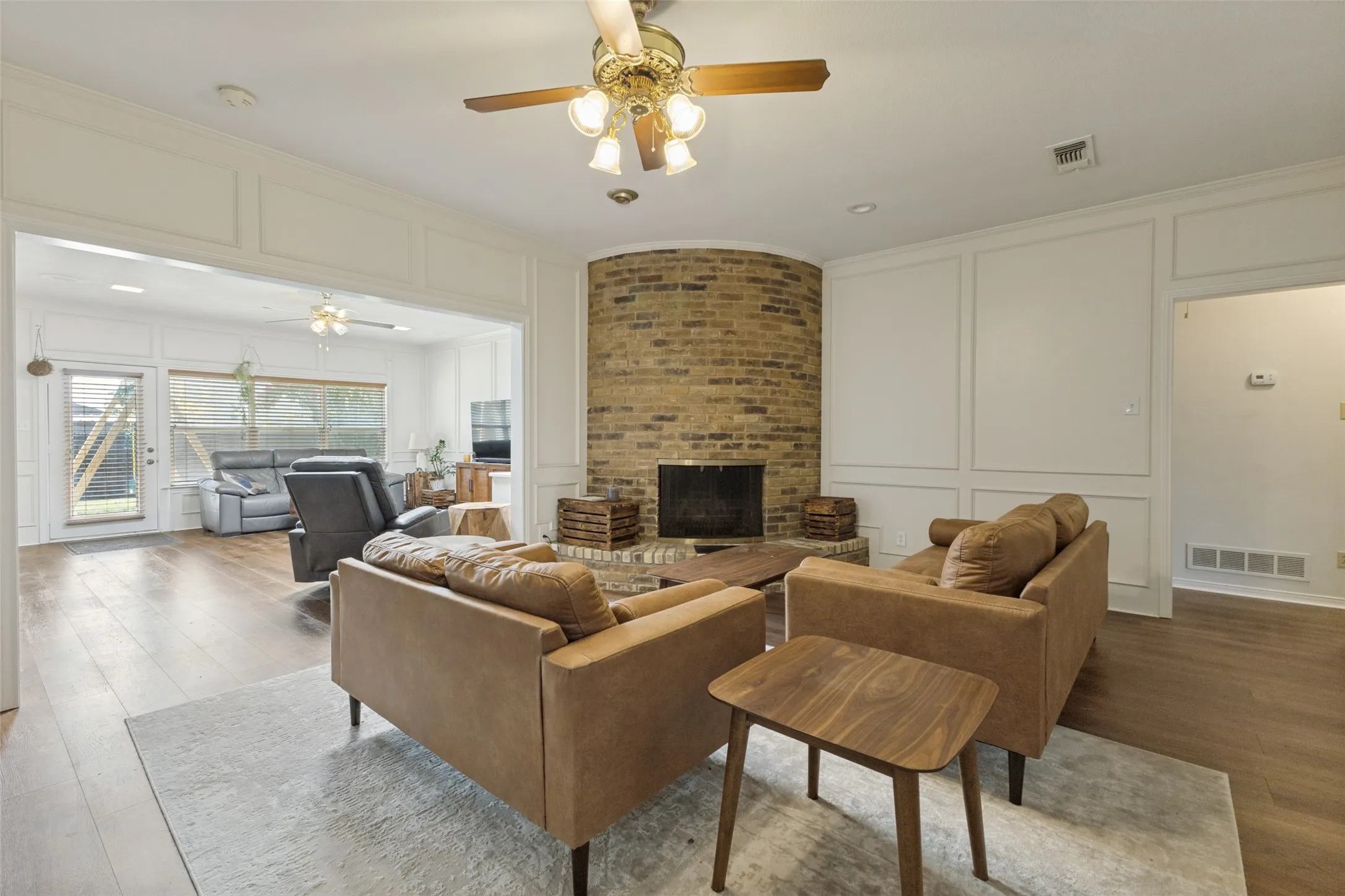 Living area featuring a brick fireplace, wood-finish flooring, white paneled walls, and a recessed lighting