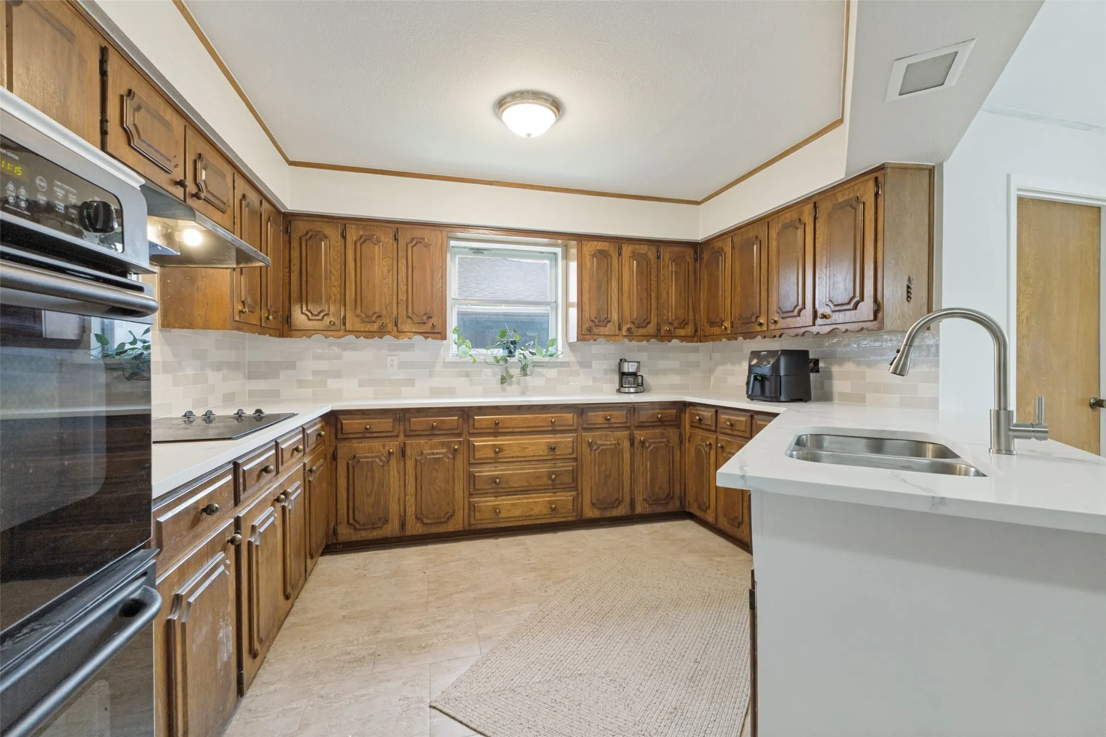 U-shaped kitchen featuring wood cabinetry, light-toned countertops, and a subway tile backsplash