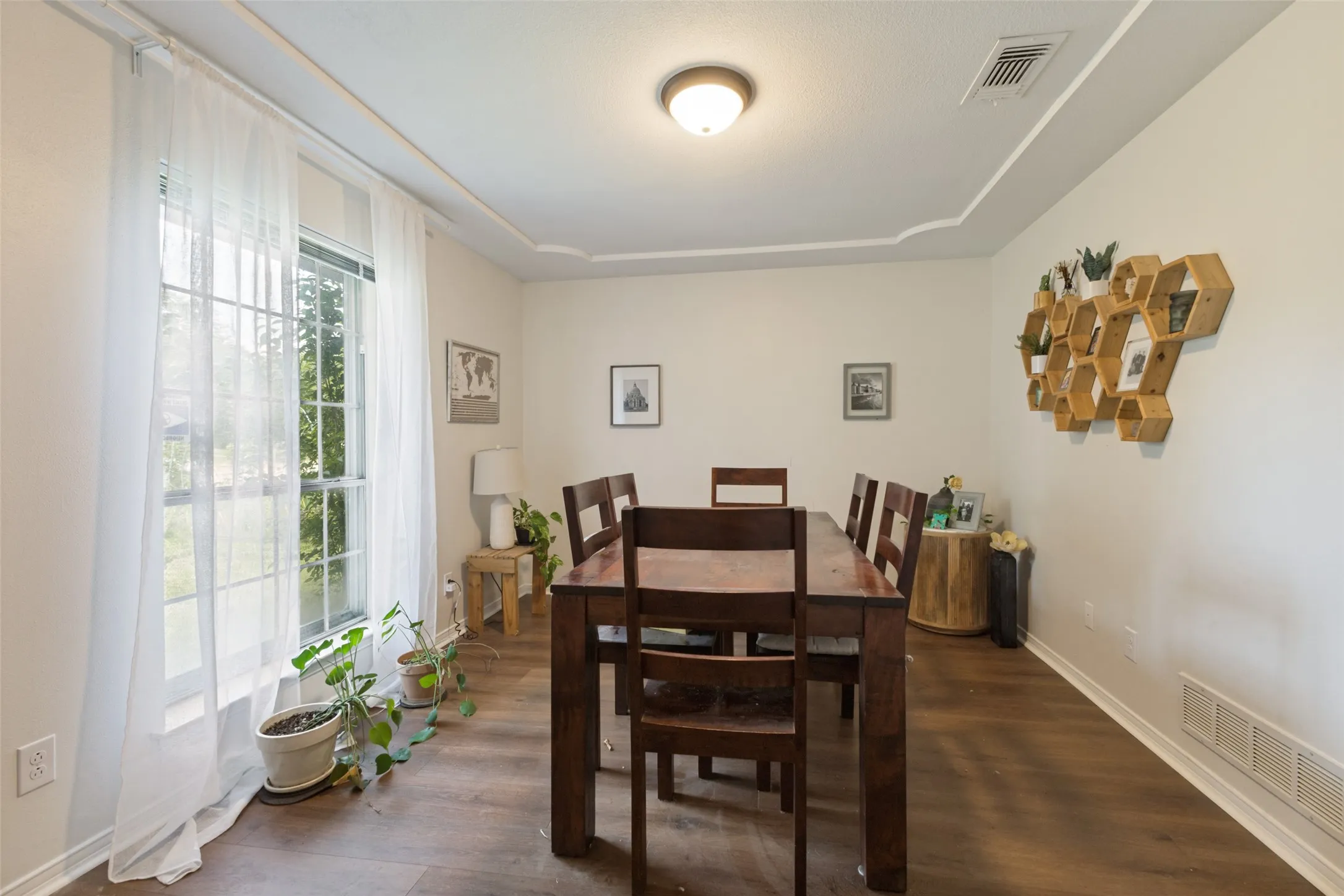 Spacious room featuring wood-finish flooring, a large window with natural light, and a tray ceiling detail