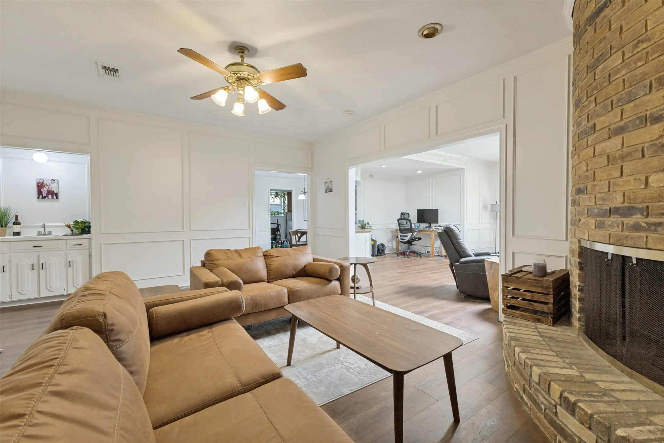 Living area featuring a brick fireplace with a metal screen, wood-finish flooring, and white paneled walls