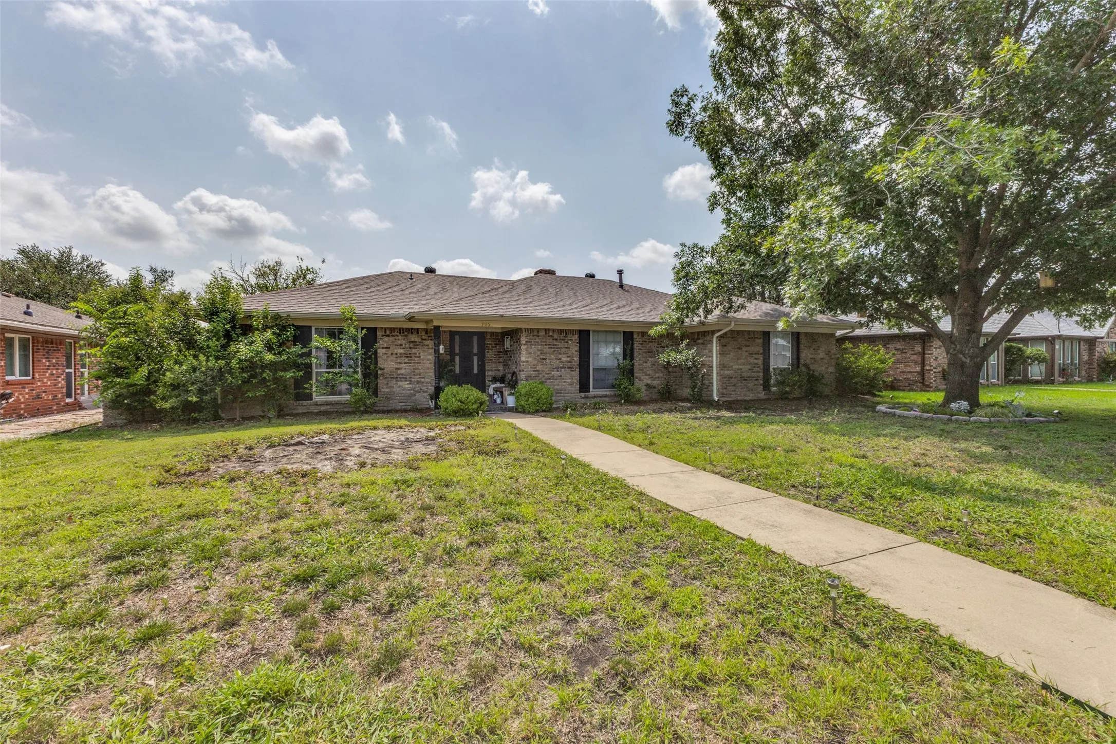 Single-story brick exterior featuring a dark front door, multiple windows with dark shutters, and a sloped roofline