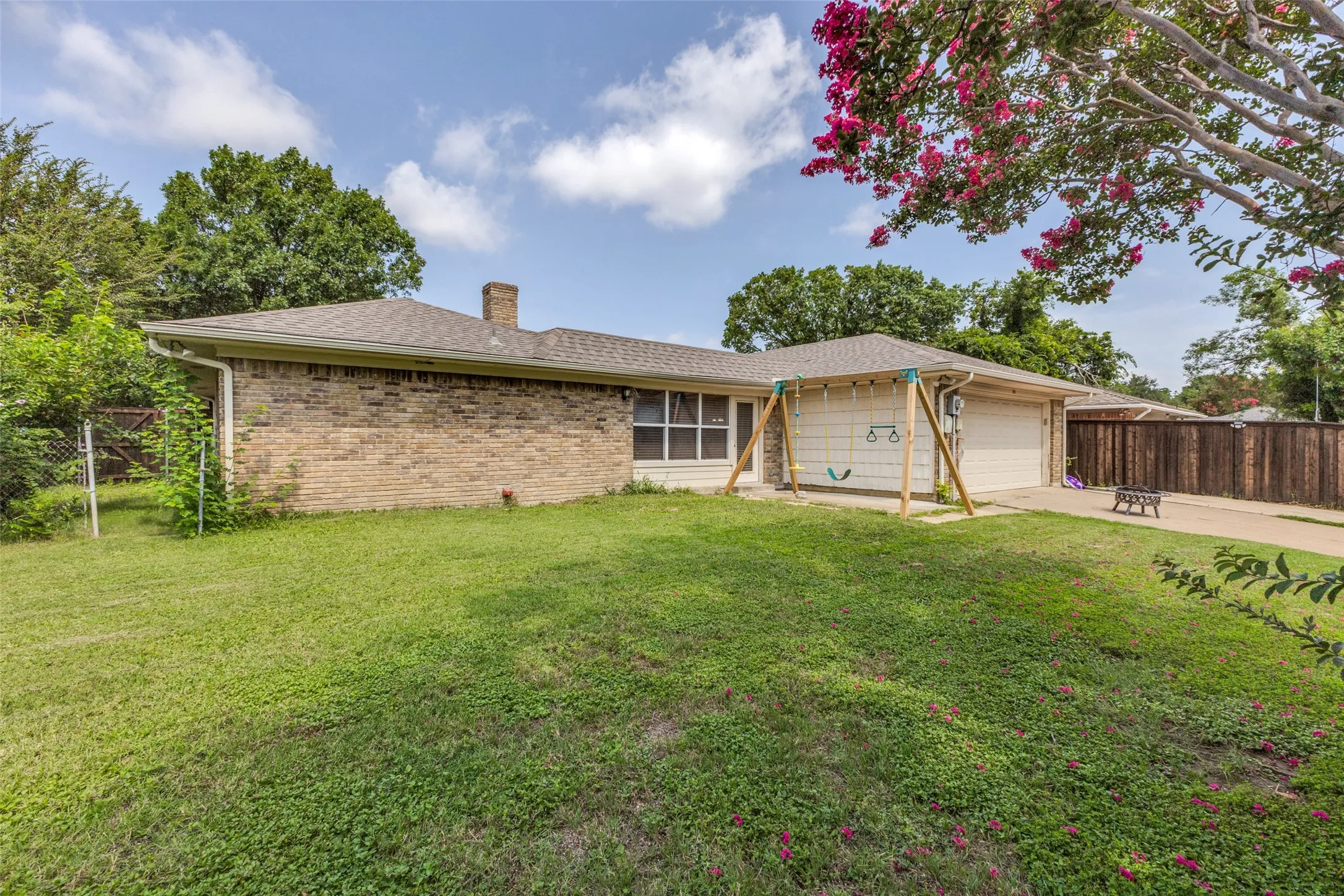 Brick exterior with an attached two-car garage, featuring a paved driveway, a green lawn, and a privacy fence