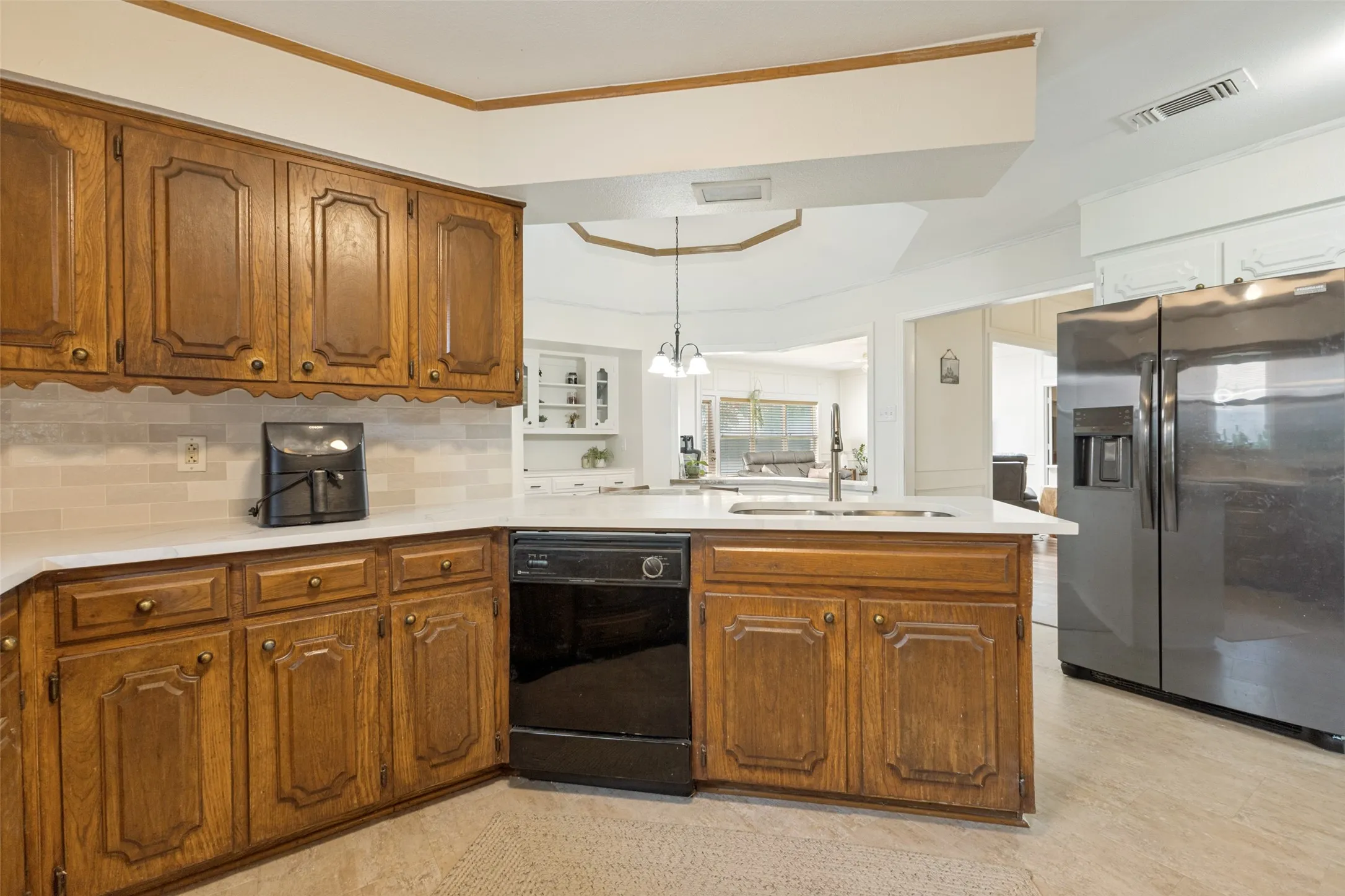 Kitchen featuring wood cabinetry, light countertops, subway tile backsplash, and a stainless steel refrigerator