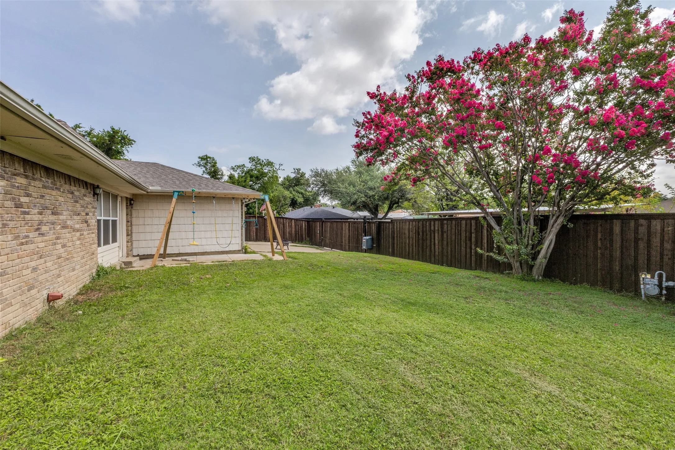 Spacious backyard featuring a manicured lawn, a mature flowering tree, and a robust privacy fence