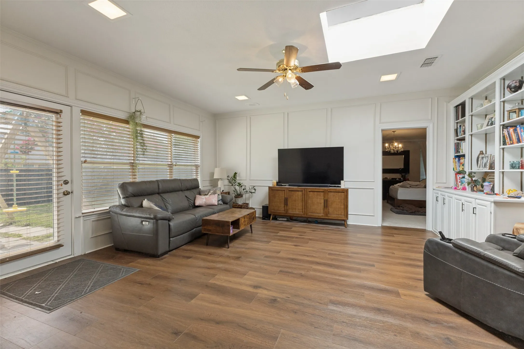 Spacious living area featuring wood-finish flooring, white paneling, and a built-in shelving unit with lower cabinetry