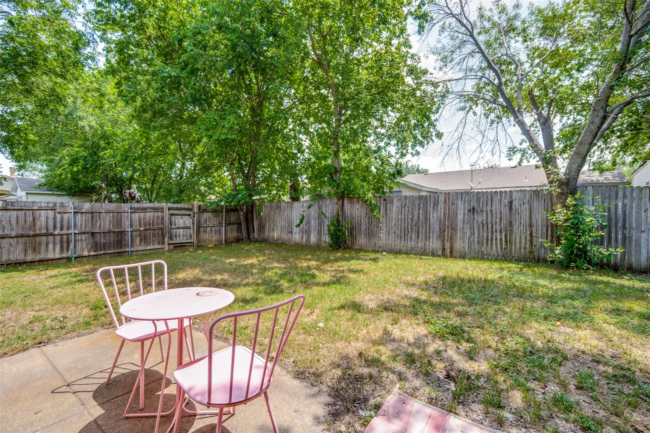Private backyard featuring a concrete patio, mature perimeter trees, and a full wooden privacy fence