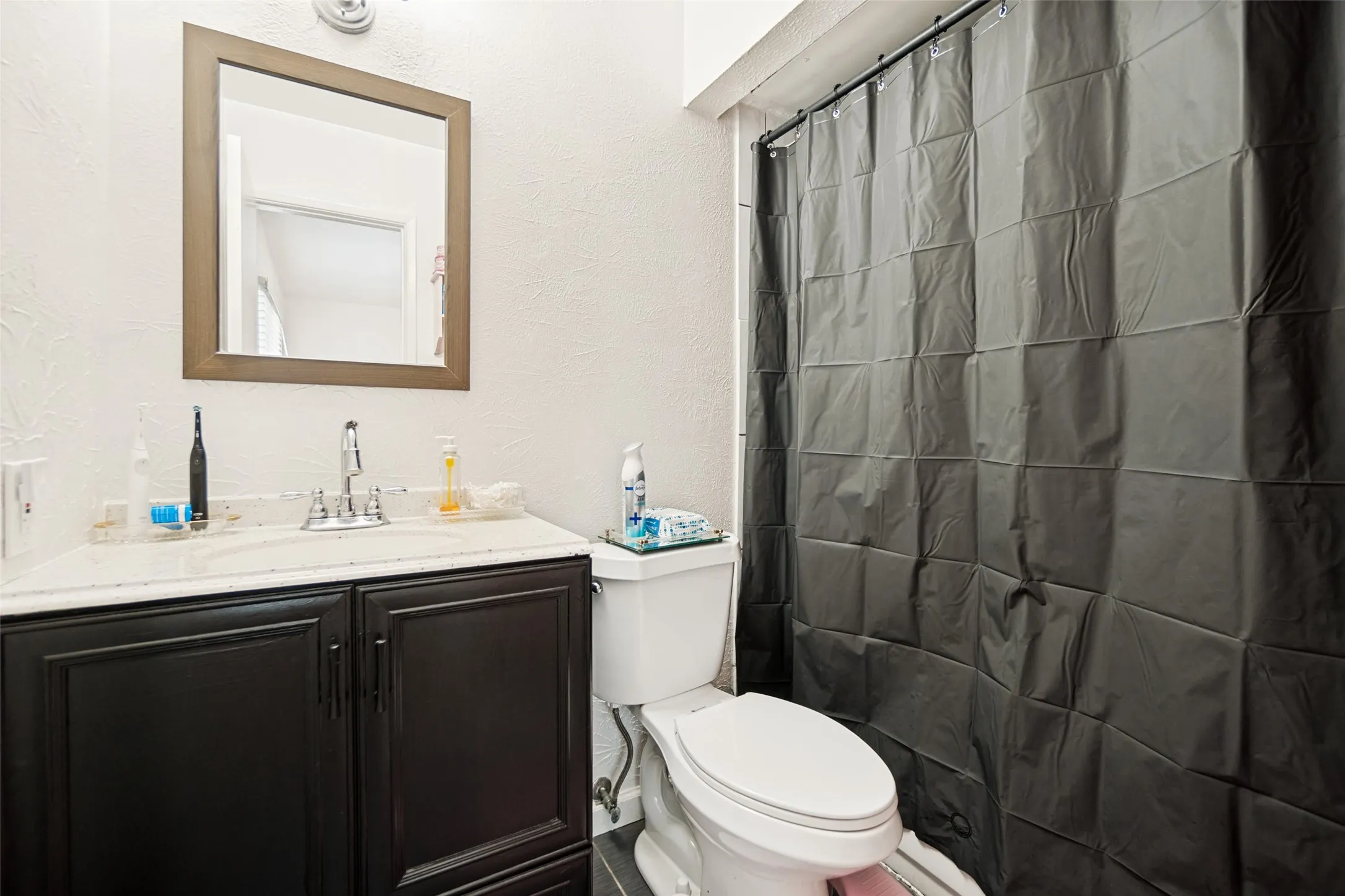 Bathroom featuring a dark wood-finish vanity with a light-colored countertop, chrome faucet, and a wall-mounted mirror