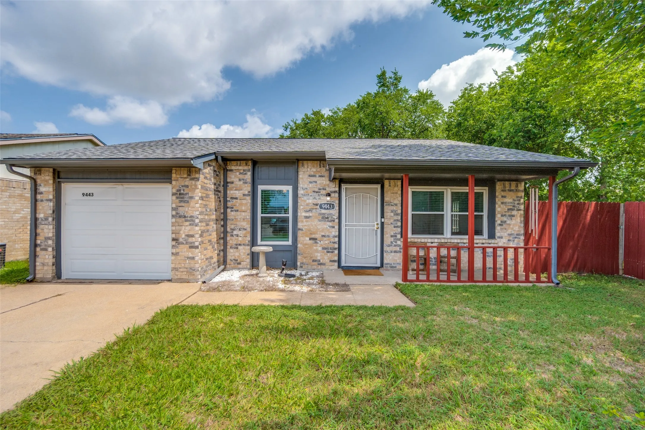 Brick facade home featuring an attached single-car garage and a covered front porch with red railing