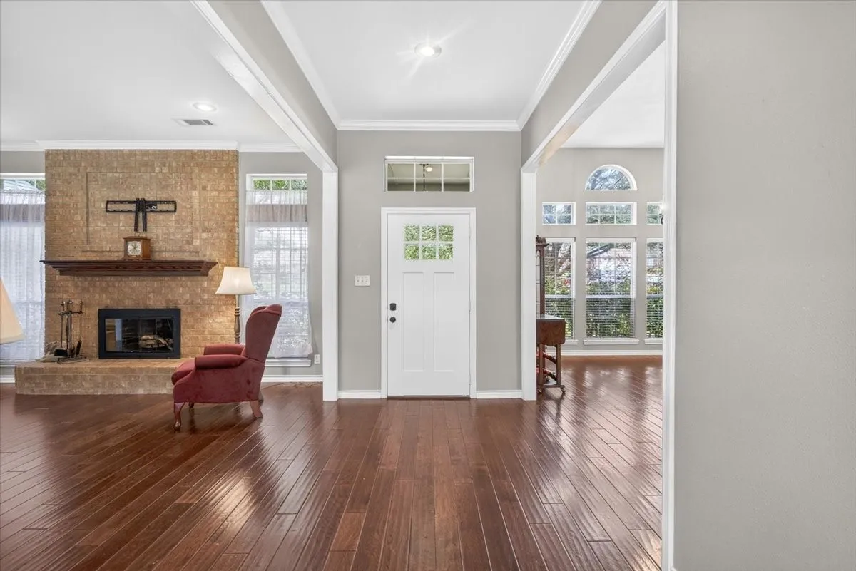 Warm wood-finish flooring extends throughout this interior, featuring a prominent brick fireplace with a wood mantel