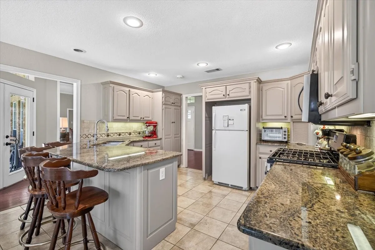 Bright kitchen featuring a multi-tone granite island and countertops, a tile backsplash, and recessed lighting