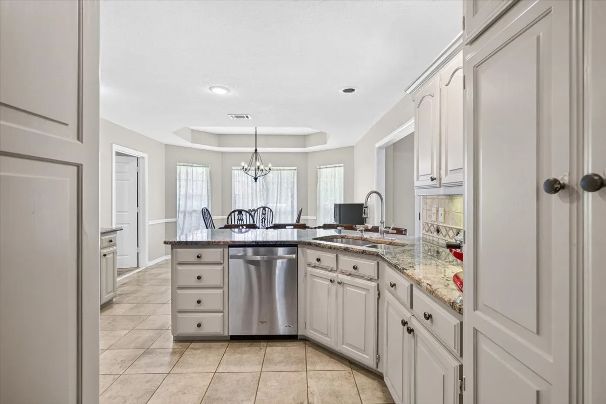Kitchen featuring a center island with a stainless steel dishwasher, a single basin sink with a high-arc faucet, granite countertops, and light-toned cabinetry