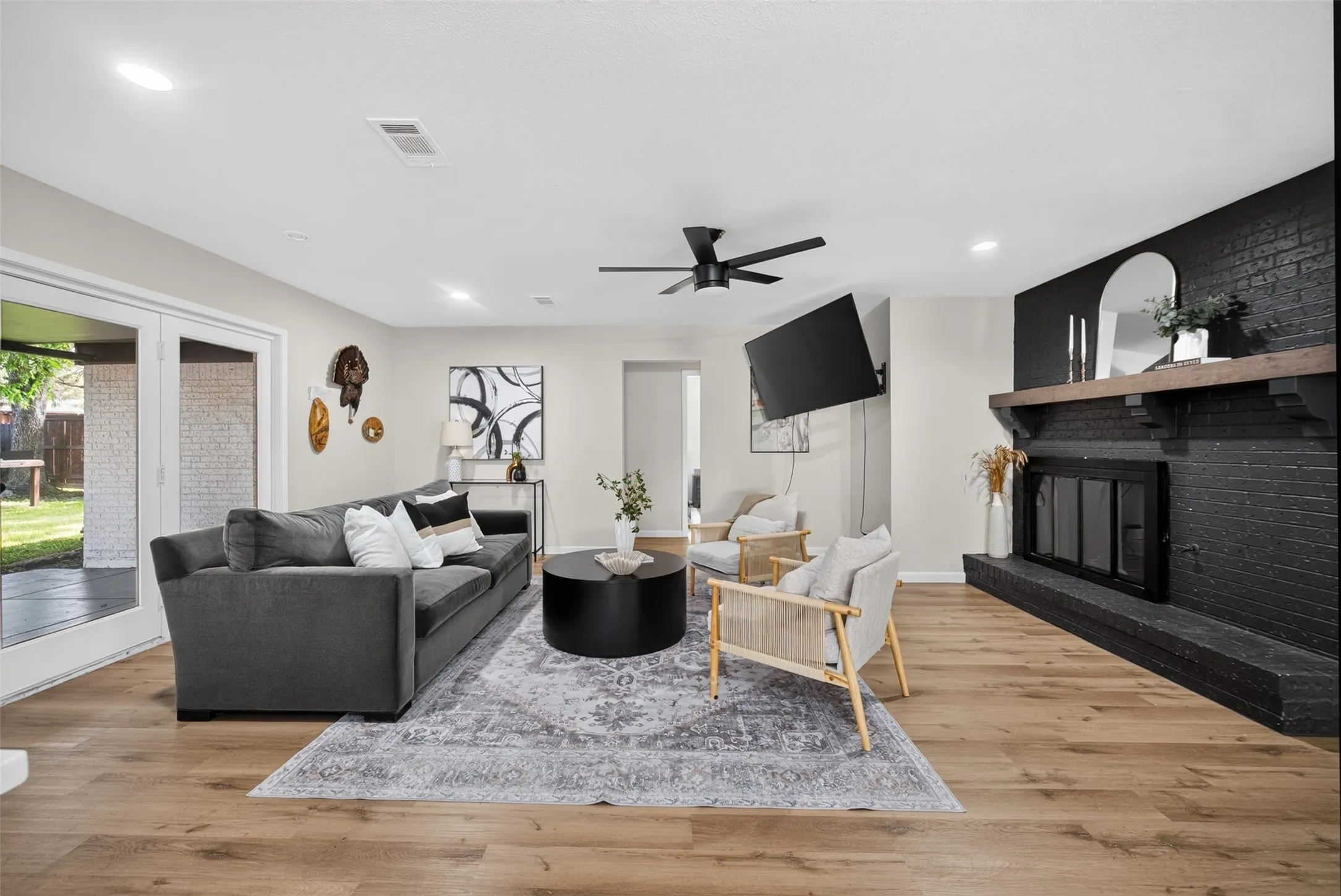 Living area featuring wood-finish flooring, a black brick fireplace with a wood mantel, and ceiling fan
