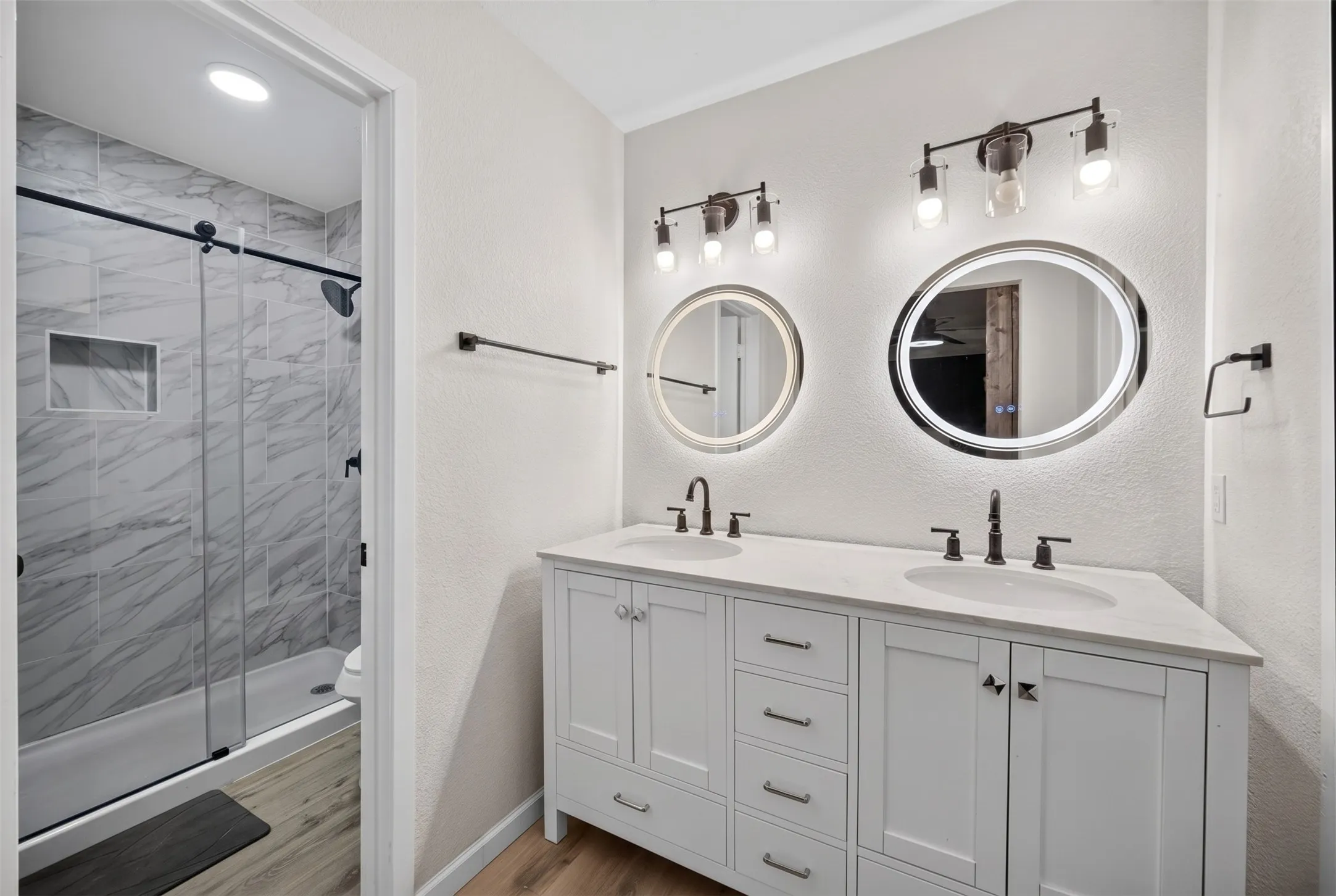 Dual vanity with white cabinetry, integrated sinks, and individual backlit circular mirrors