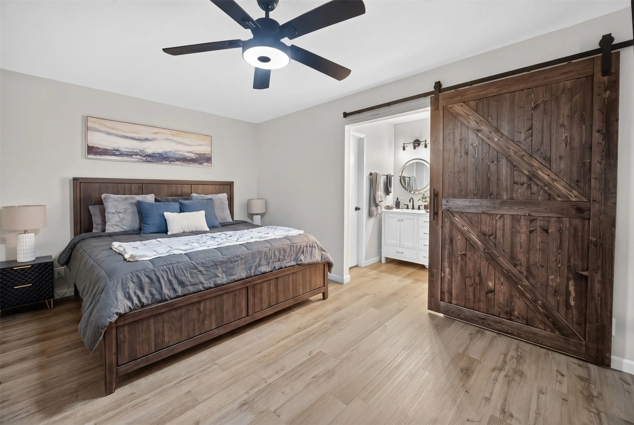 Bedroom featuring wood-finish flooring, a ceiling fan with integrated lighting, and a dark wood barn door