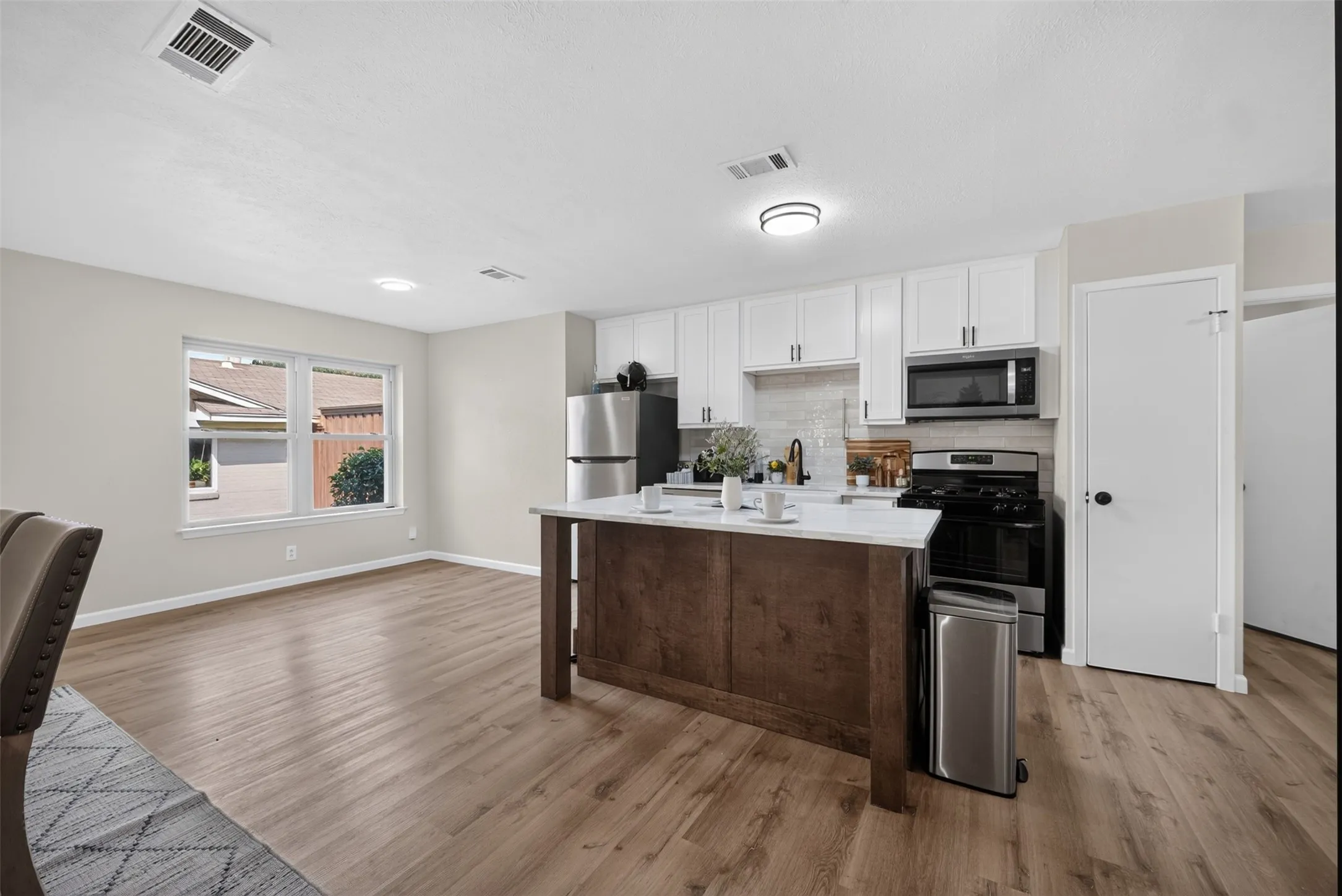 Open-concept kitchen featuring white cabinetry, a central island with a light-toned countertop, and stainless steel appliances