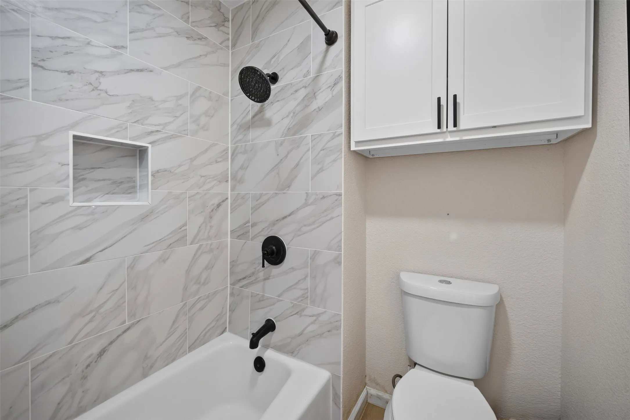 Tub and shower with marbled tile surround, featuring matte black fixtures and a recessed niche