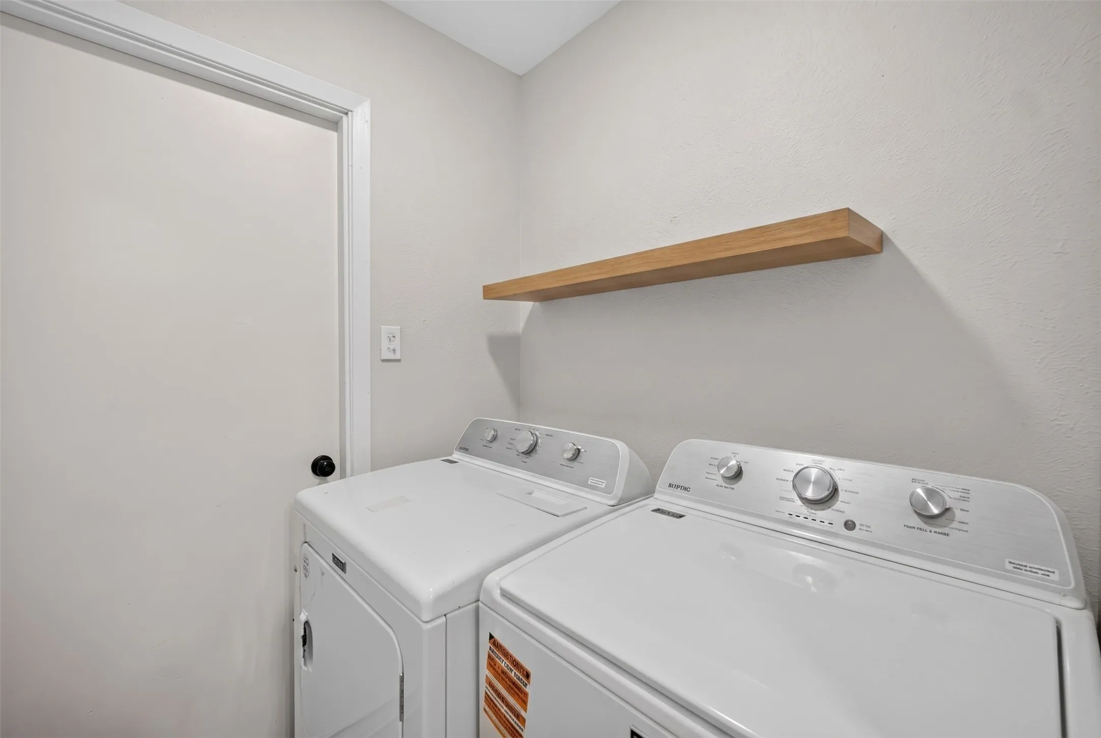 Laundry area featuring a floating wood-finish shelf and a light-colored wall finish