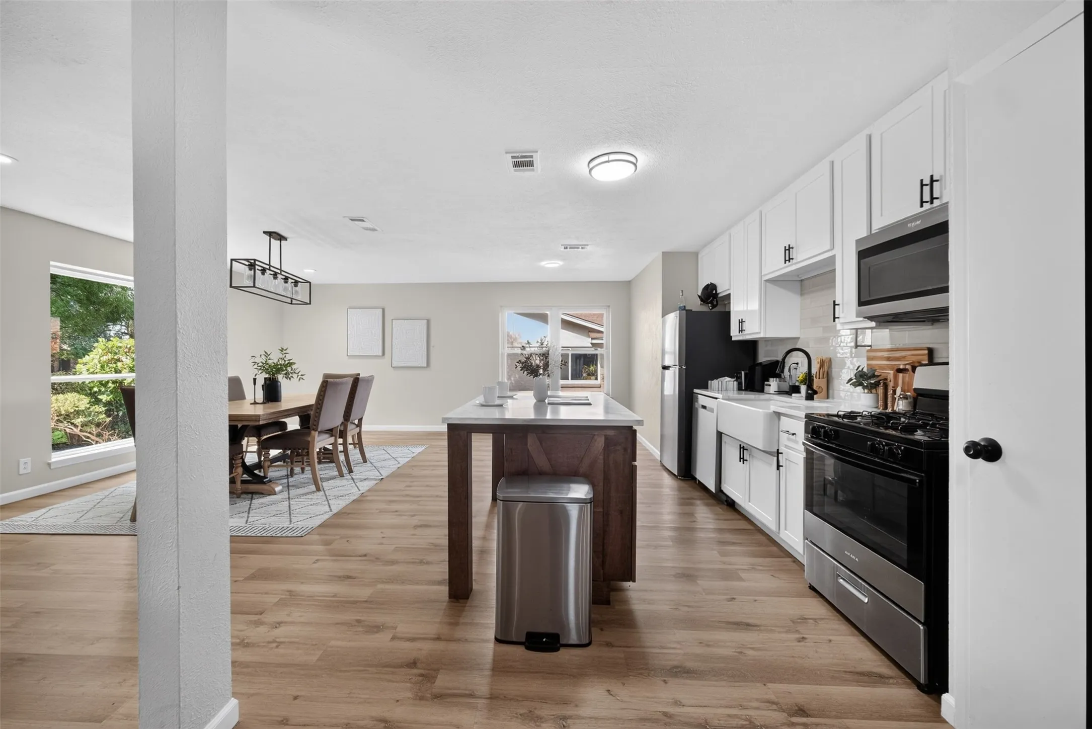 Modern kitchen featuring white shaker cabinetry, stainless steel appliances, a farmhouse sink, and wood-finish flooring