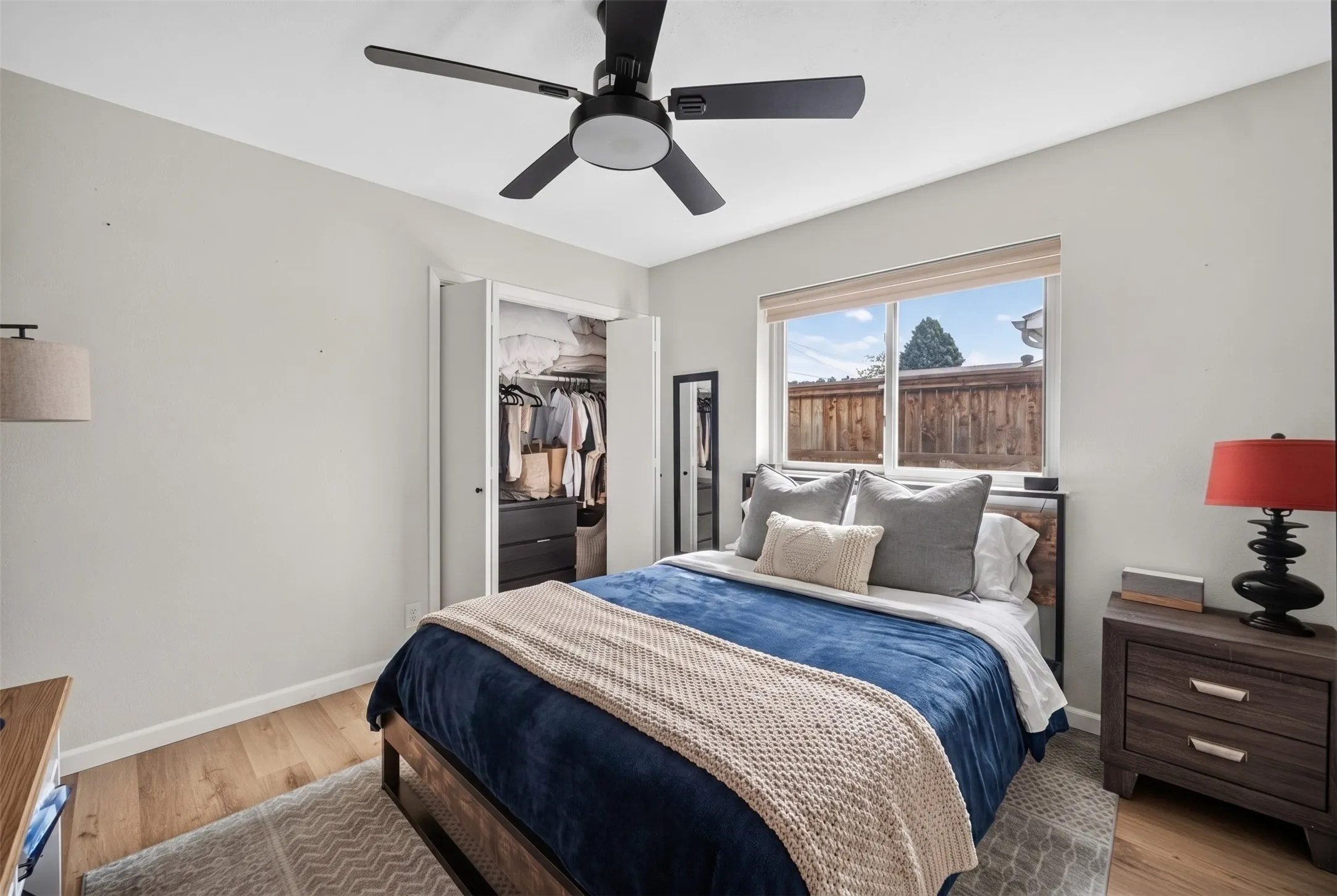 Bedroom featuring light wood-finish flooring, a ceiling fan with integrated lighting, a built-in closet with bifold doors, and a large window