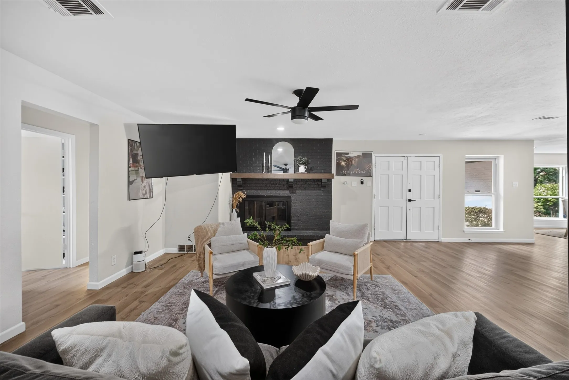 Spacious living area featuring wood-finish flooring, a contemporary ceiling fan, and a black brick fireplace with a wood mantle