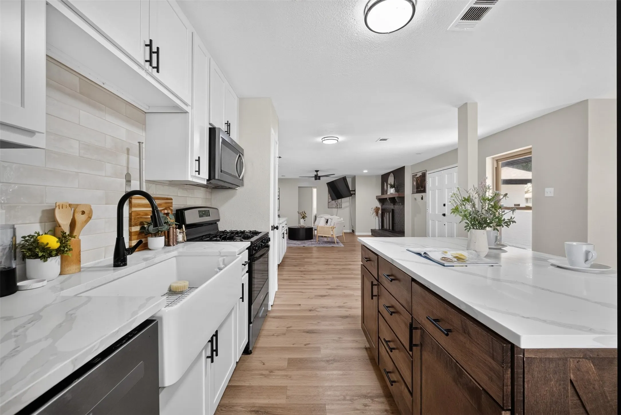 Kitchen featuring white shaker cabinetry, white farmhouse sink, black hardware and fixtures, and light wood-finish flooring