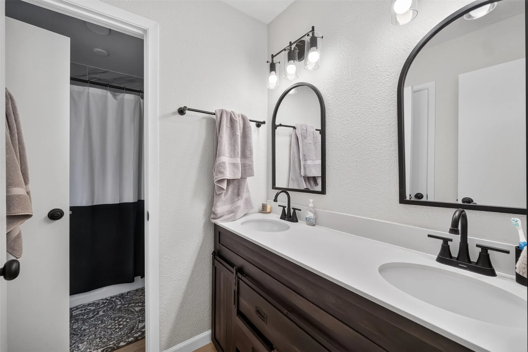 Double vanity with undermount sinks, black matte fixtures, and arched mirrors