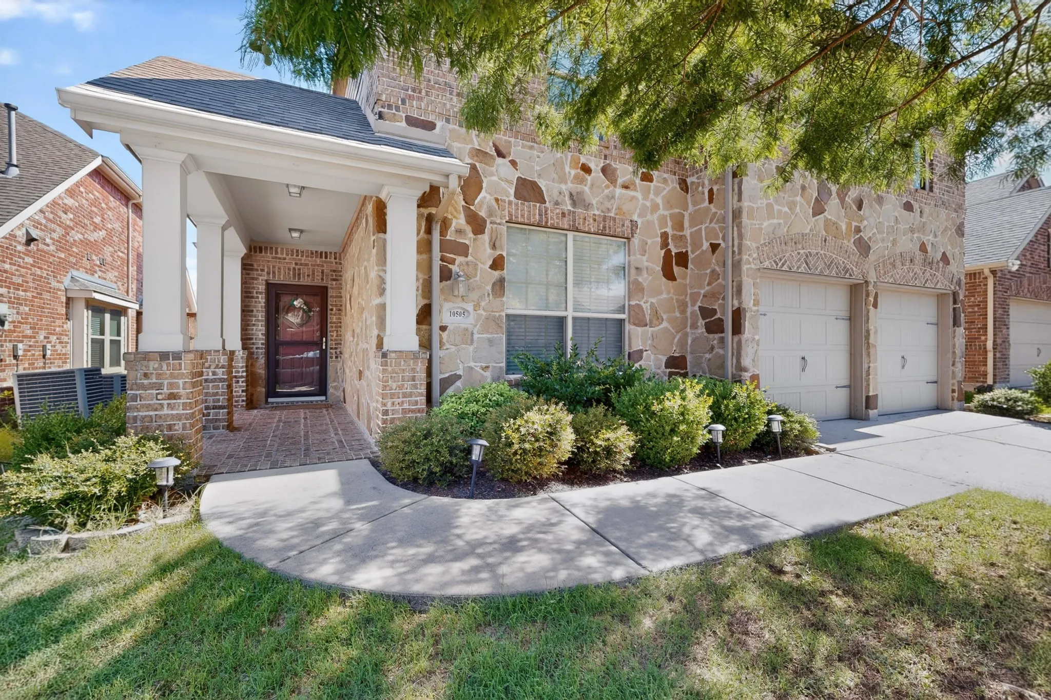 Stone and brick exterior featuring a covered front porch, dual garage doors, and a concrete driveway