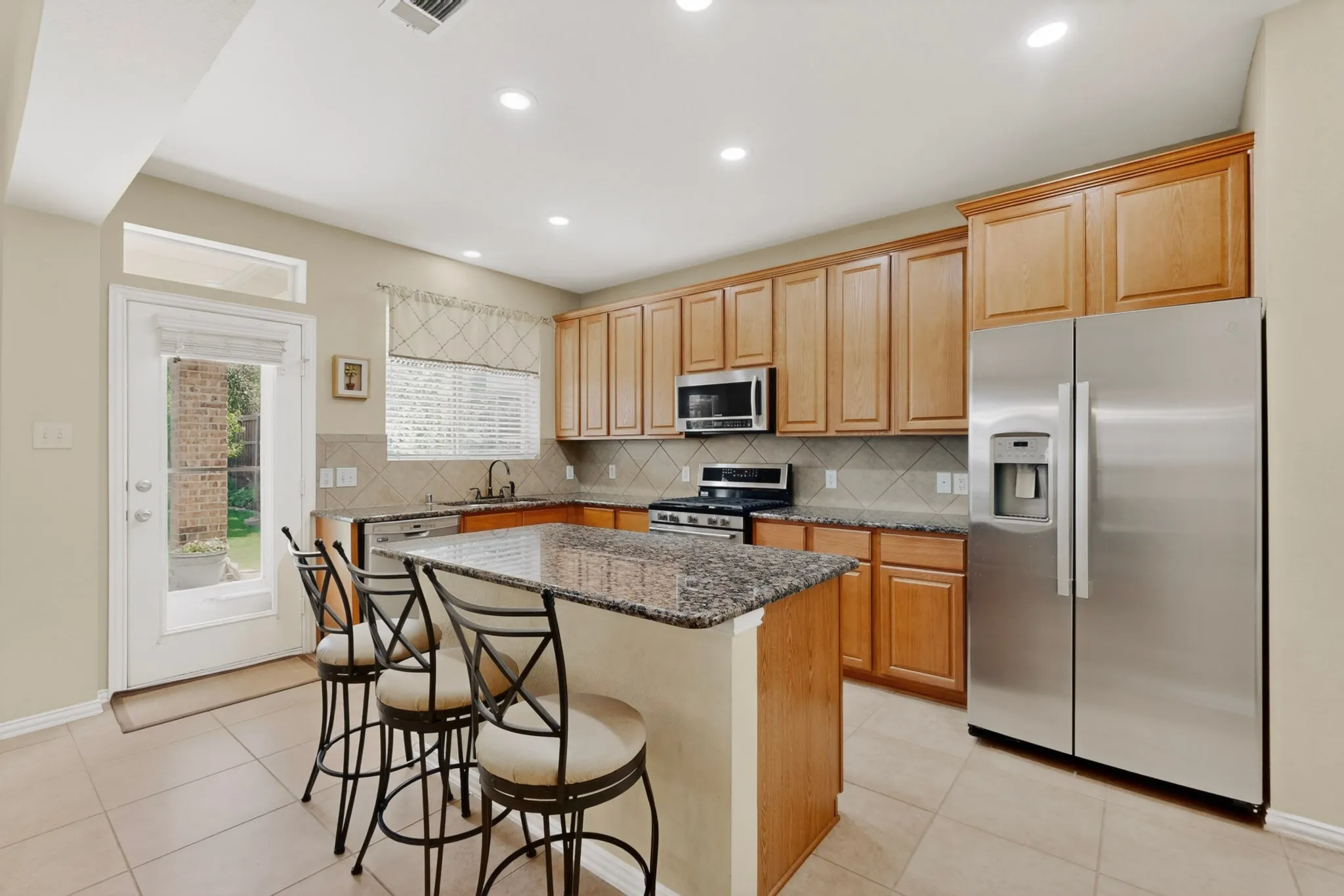 Kitchen featuring a center island with a granite countertop, wood cabinetry, stainless steel appliances, tile flooring, and recessed lighting