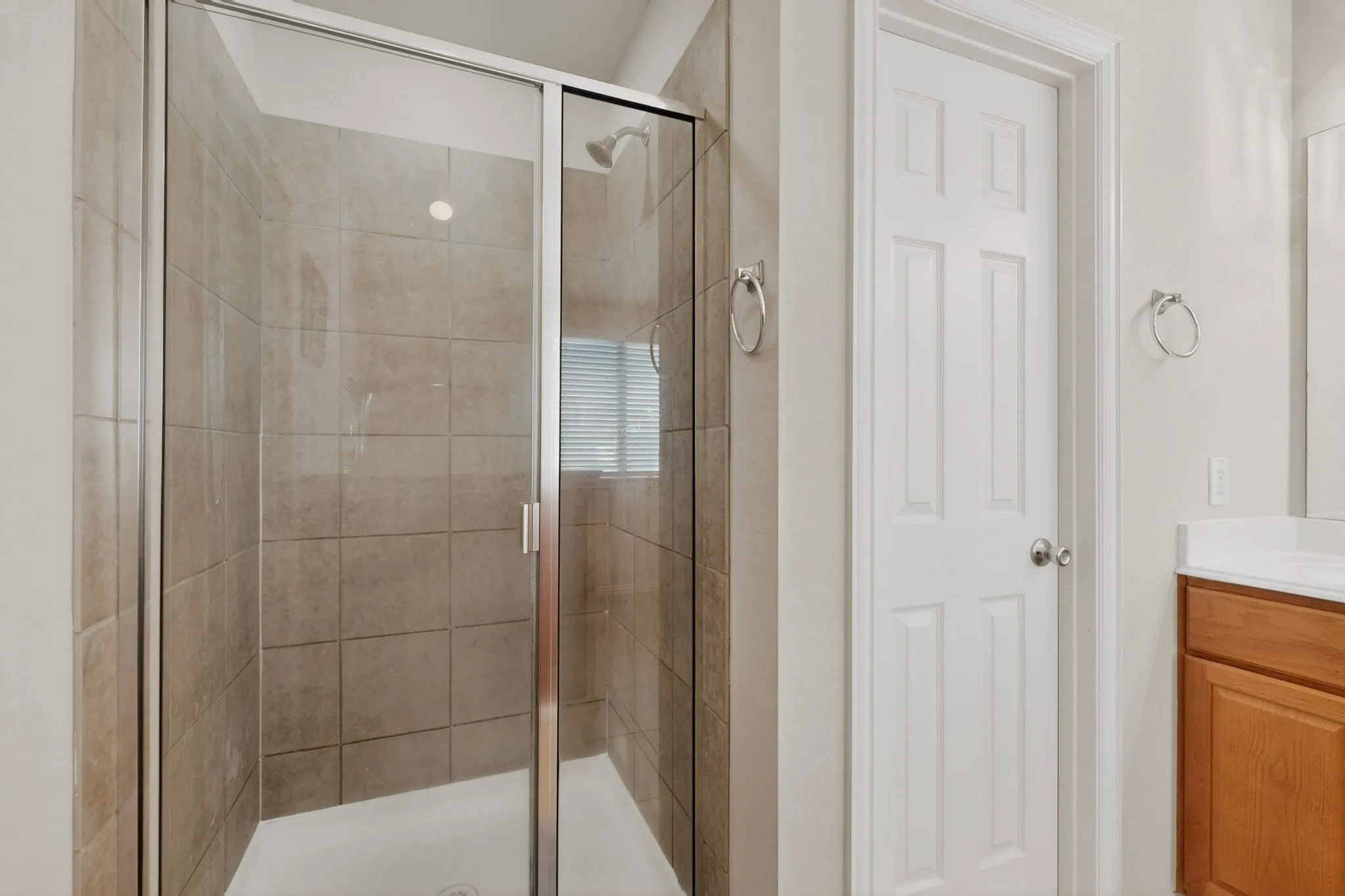 Enclosed shower with clear glass door, tiled walls, white shower pan, and a single shower head