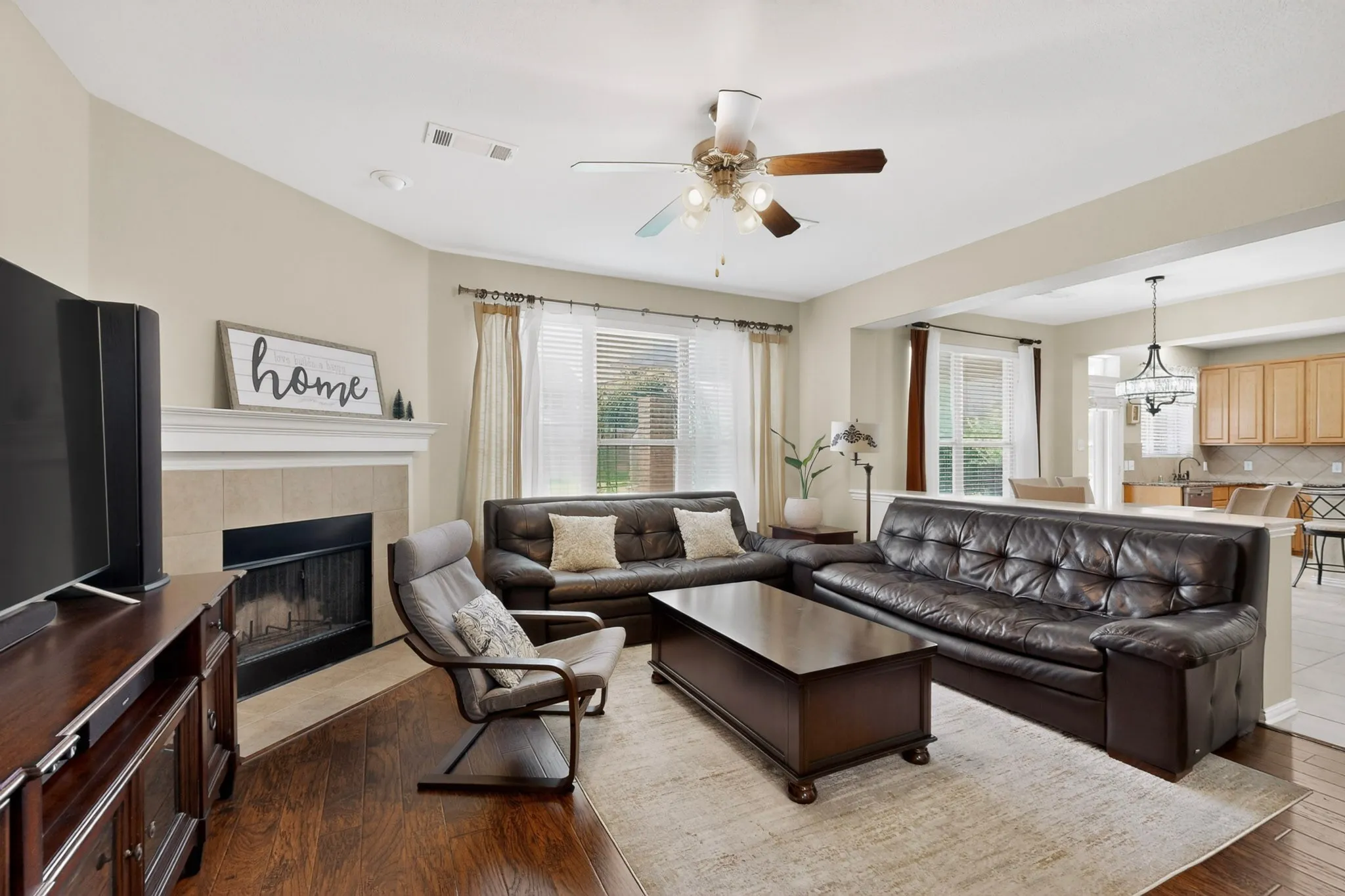 Spacious living area featuring wood-finish flooring, a ceiling fan with integrated lighting, and a fireplace with a stone surround and mantle