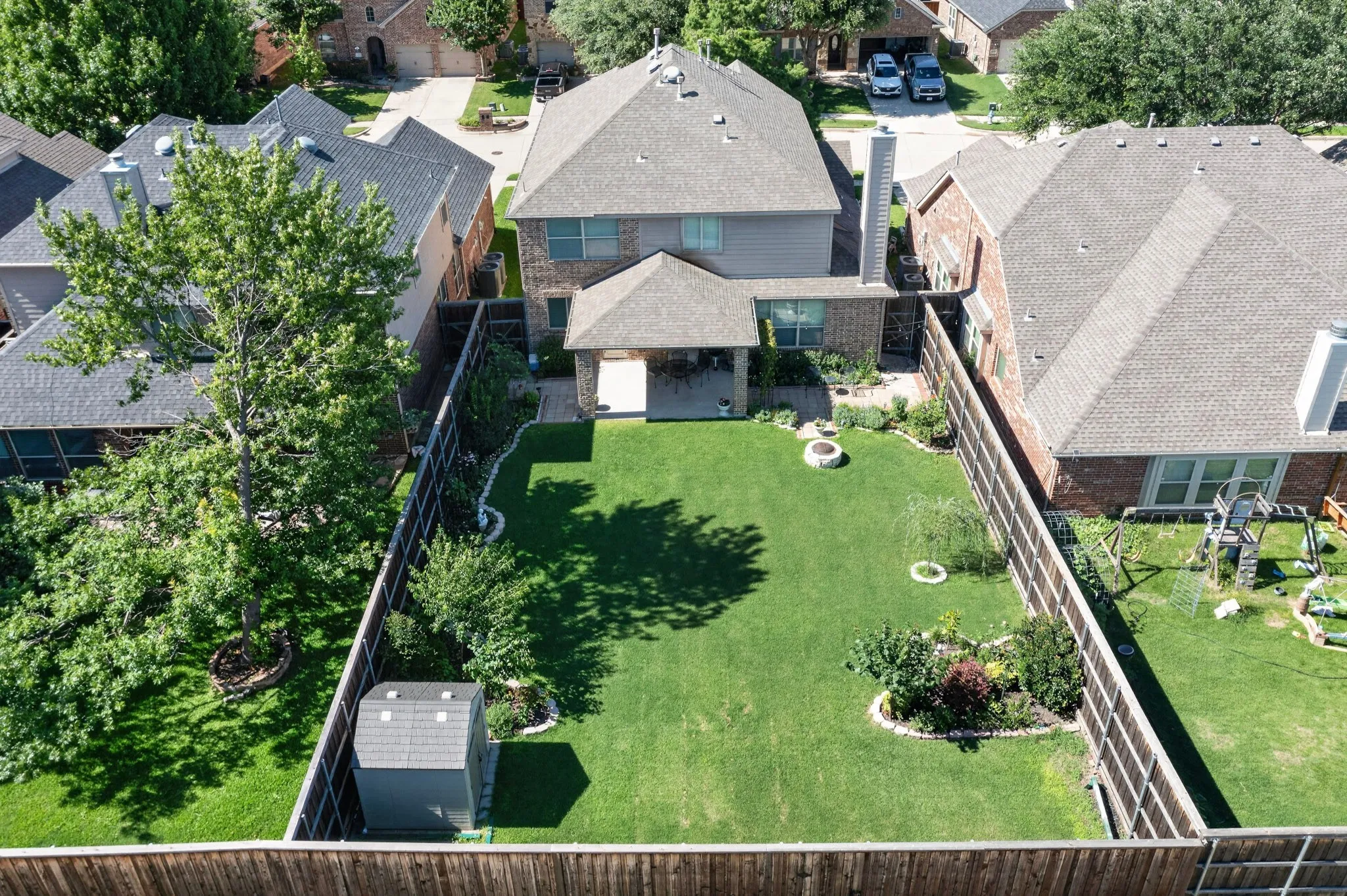Spacious backyard featuring a manicured lawn, established landscaping beds, a covered patio, and a storage shed