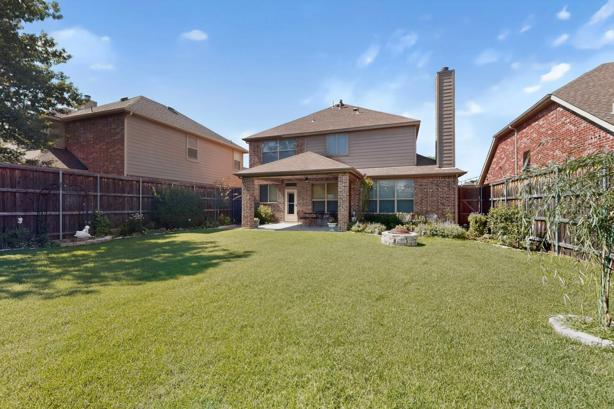 Spacious backyard featuring a manicured lawn, a covered patio, and a stone fire pit