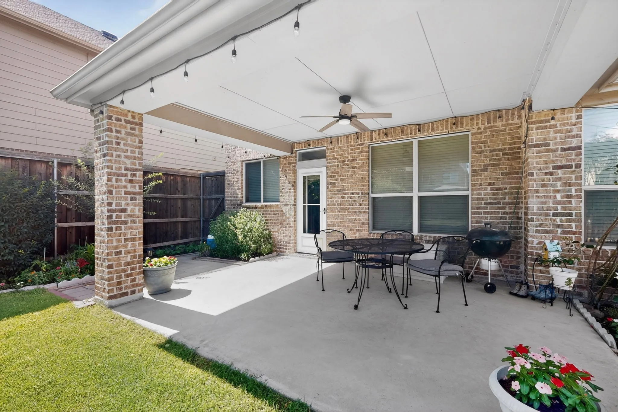 Covered patio featuring a ceiling fan, string lighting, and brick support columns