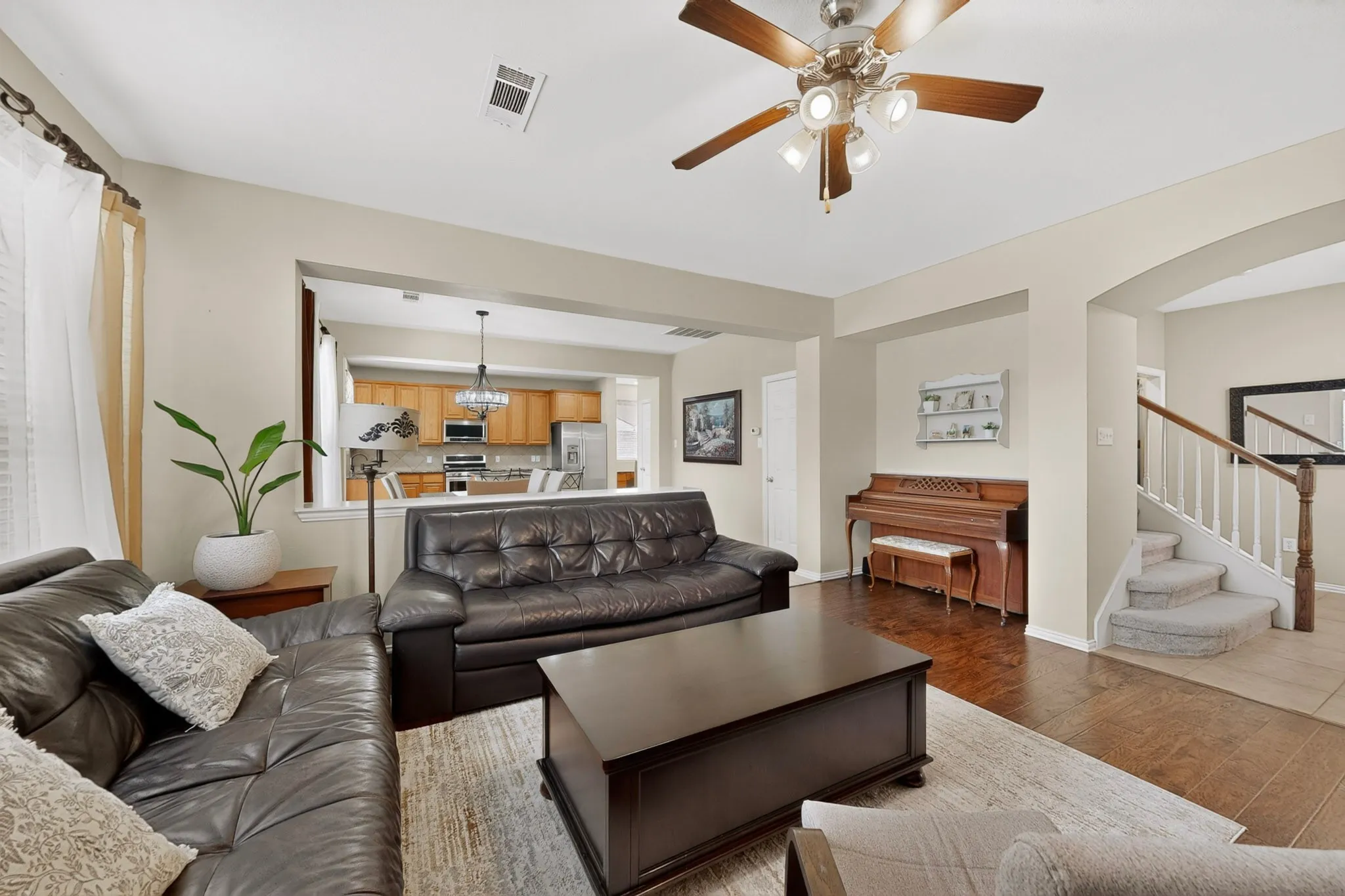 Living area featuring wood-finish flooring, a ceiling fan with integrated lighting, and an archway leading to a carpeted staircase with white balusters and a wood handrail