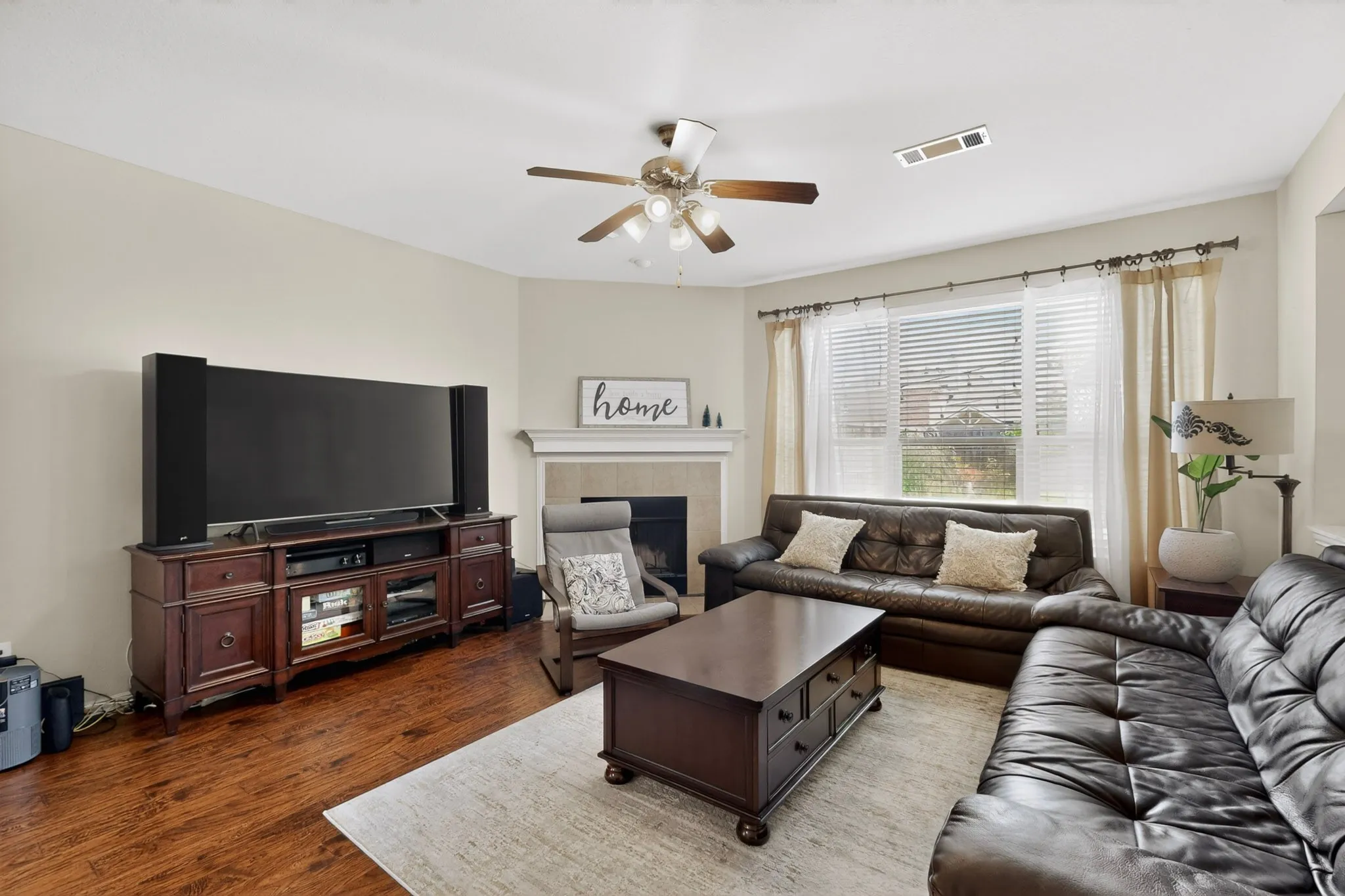 Living area featuring wood-finish flooring, a ceiling fan, and a fireplace with a mantel